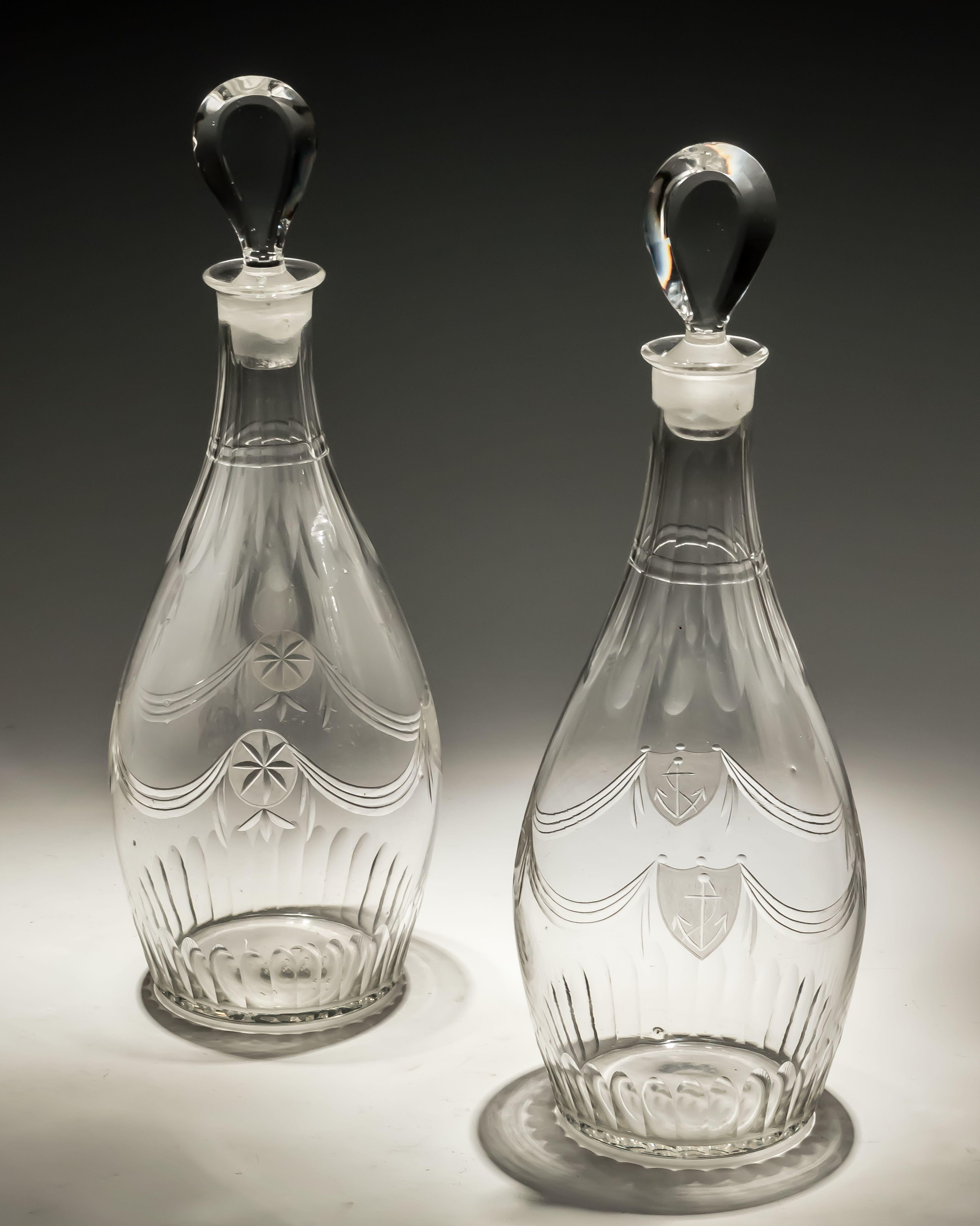 A suite of late 18th century Adam period cut glass, comprising of two club shaped decanters with tear drop stoppers, and five conical stem glasses, all finely engraved with swags, frosted stars and shields with anchors suggesting a nautical