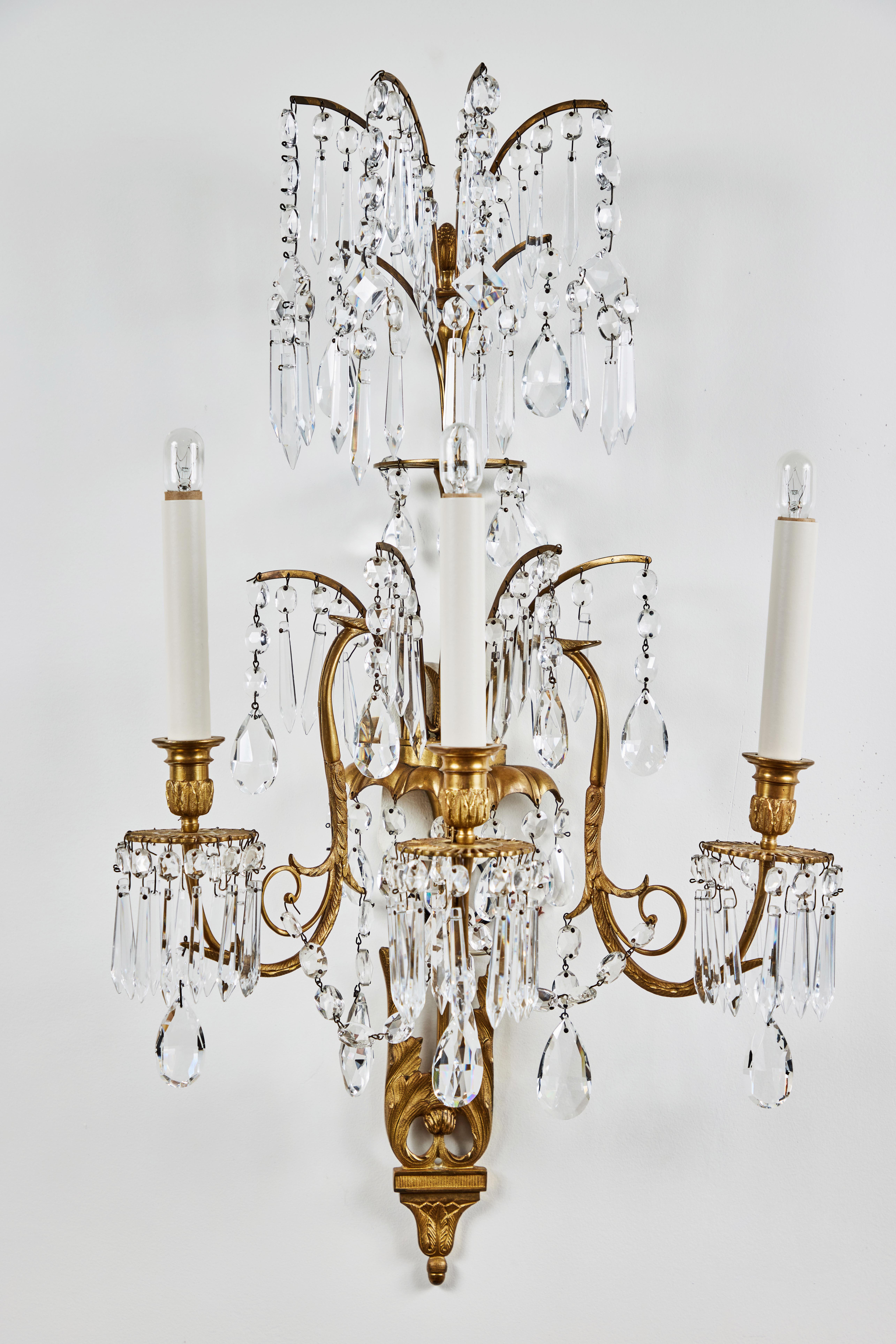 Two pairs of glamorous, circa 1930, Russian wall sconces in gilt bronze frames embellished with foliate forms. Each with three, dramatic illuminated arms, and crowned by splayed fronds. All richly embellished with cut crystal drops throughout. Wired