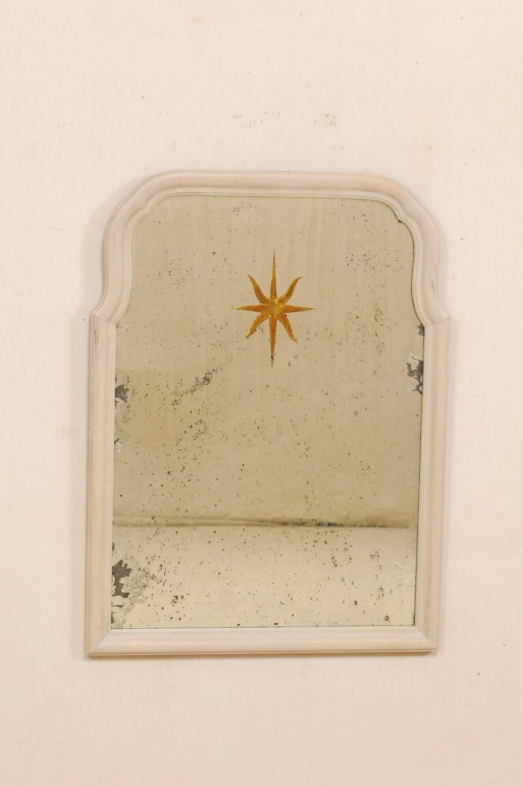 An American églomisé mirror with sunburst center. This vintage mirror features a light, neutral toned wooden surround, with convex arch top, and aged glass within. The attention is immediately drawn to the verre églomisé star or sunburst at the