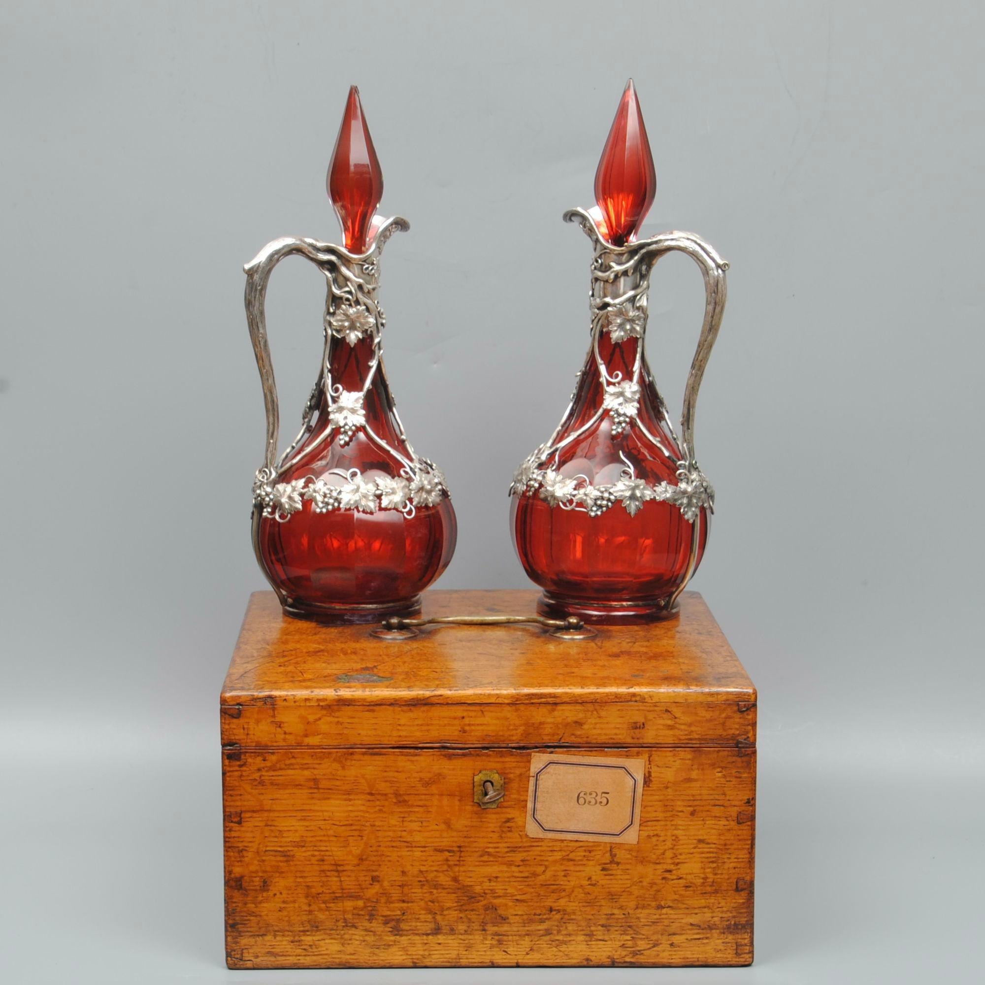 A fine pair of Ruby glass and white metal mounted claret jugs and stoppers (possibly by Elkingtons, sadly trade label from case is missing). The oak case is fitted to take both the jugs with separated place for the stoppers. The metal mounts and