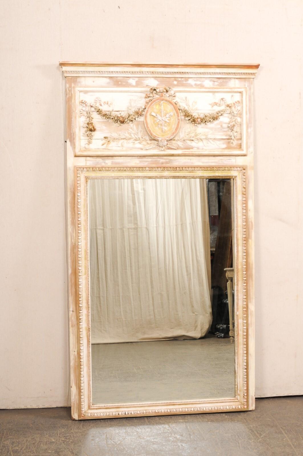 A finely detailed French Neoclassical carved-wood trumeau mirror from the 19th century. This tall antique mirror from France features the carved-wood plaque top, reminiscent of trumeau design, with linear trim molding at the top rail and lamb's
