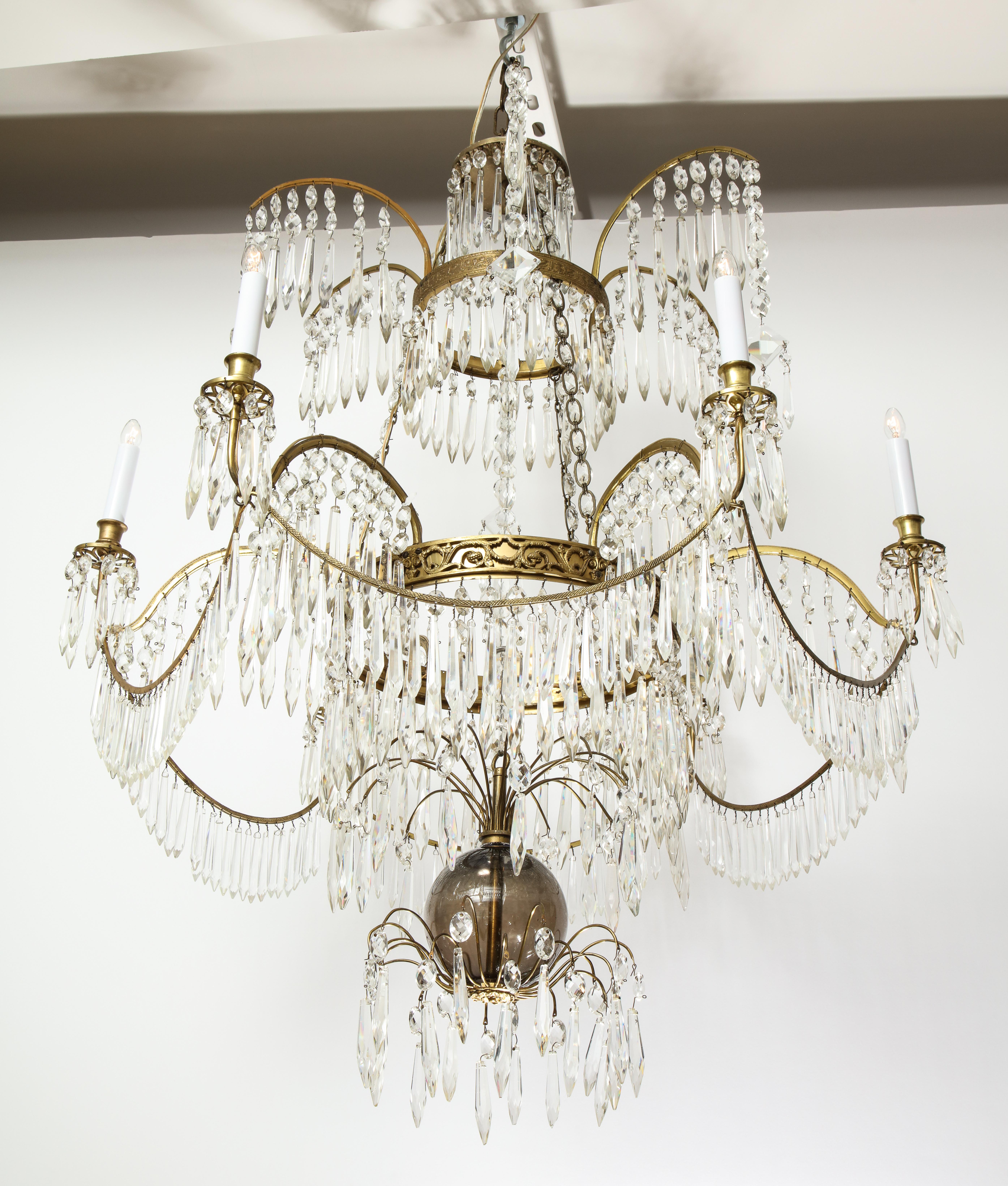 Having a central glass pendant hung by a crystal chain and surrounded by crystal drops, the upper tier having six arms hung with cascading crystal drops, the lower tier having six 