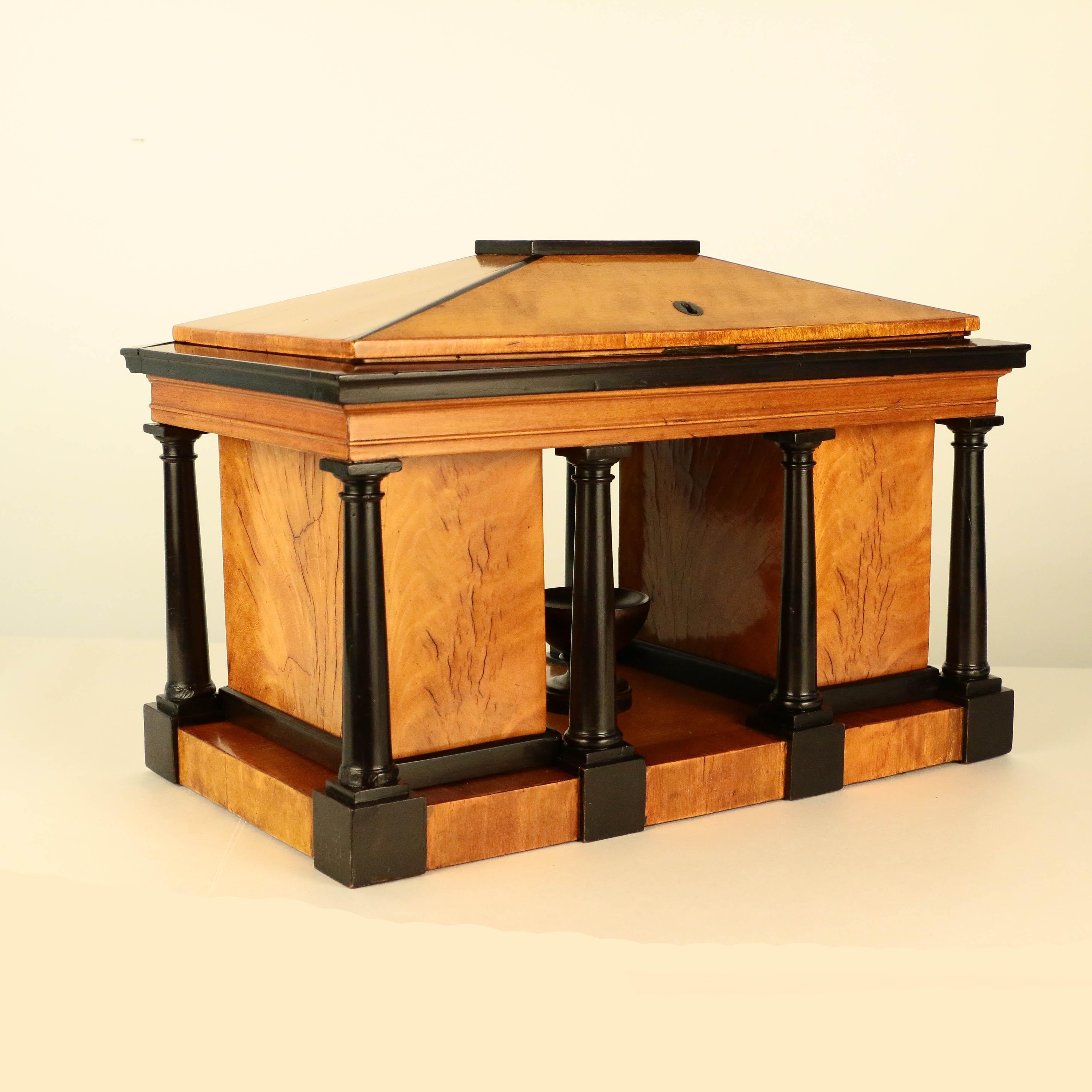 This remarkable and unique caddy is modelled after a Greek Temple with Doric columns, the panelled cover with rising top revealing two covered tea canisters, each with foil liner, the structure with eight turned columns, centred by an ebonized urn,