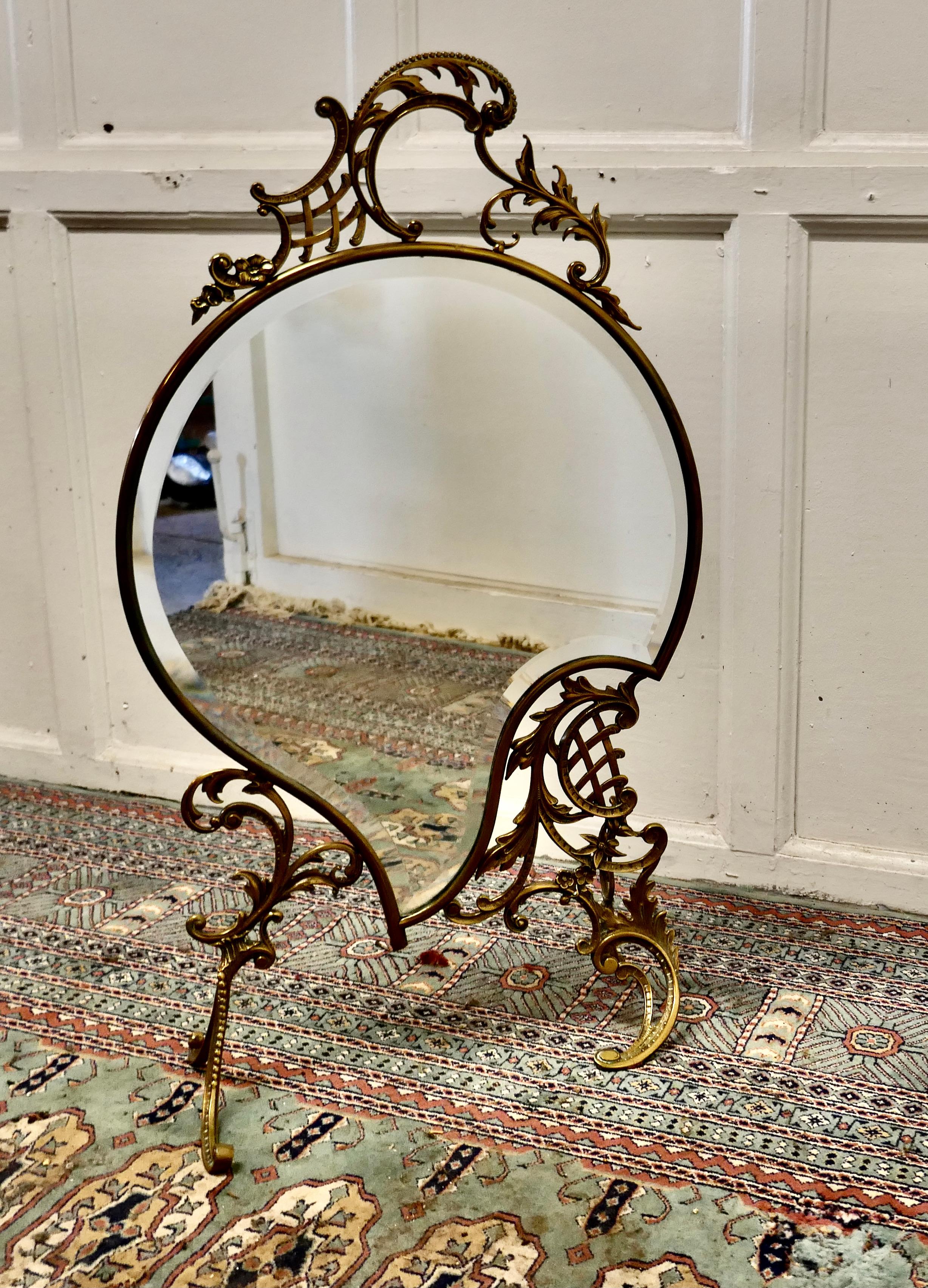 A superb French brass Rococo fire screen

The Fire screen is a superb quality piece, it is has a very unusual shape with curves and a carrying handle to the top. 
The frame is very decorative ormolu and it has a beveled mirror glass
The style is