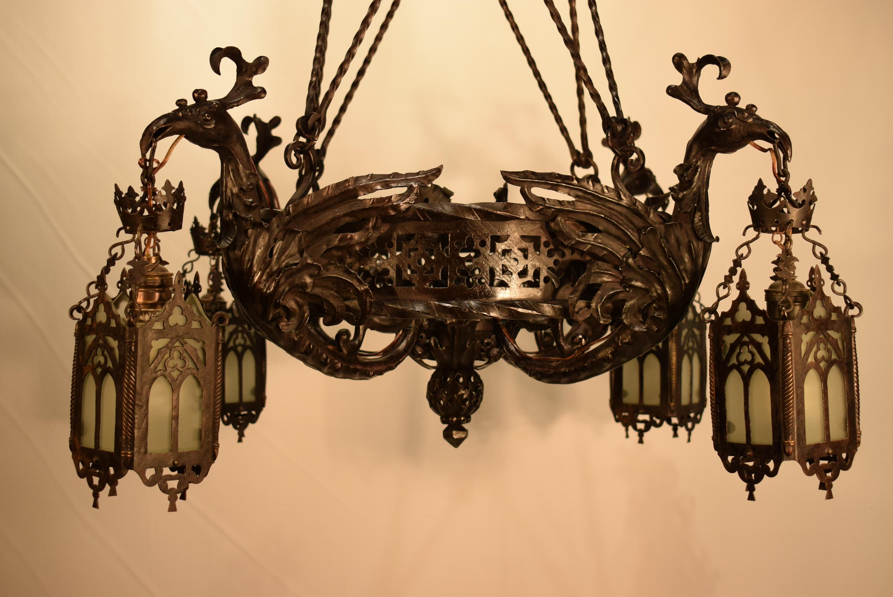 A superb iron chandelier featuring a pierced gallery issuing four stylized phoenix birds each one holding a square Gothic style lantern from its beak. Each lantern fitted with frosted glass panels. The hole suspended by eight twisted rods, later
