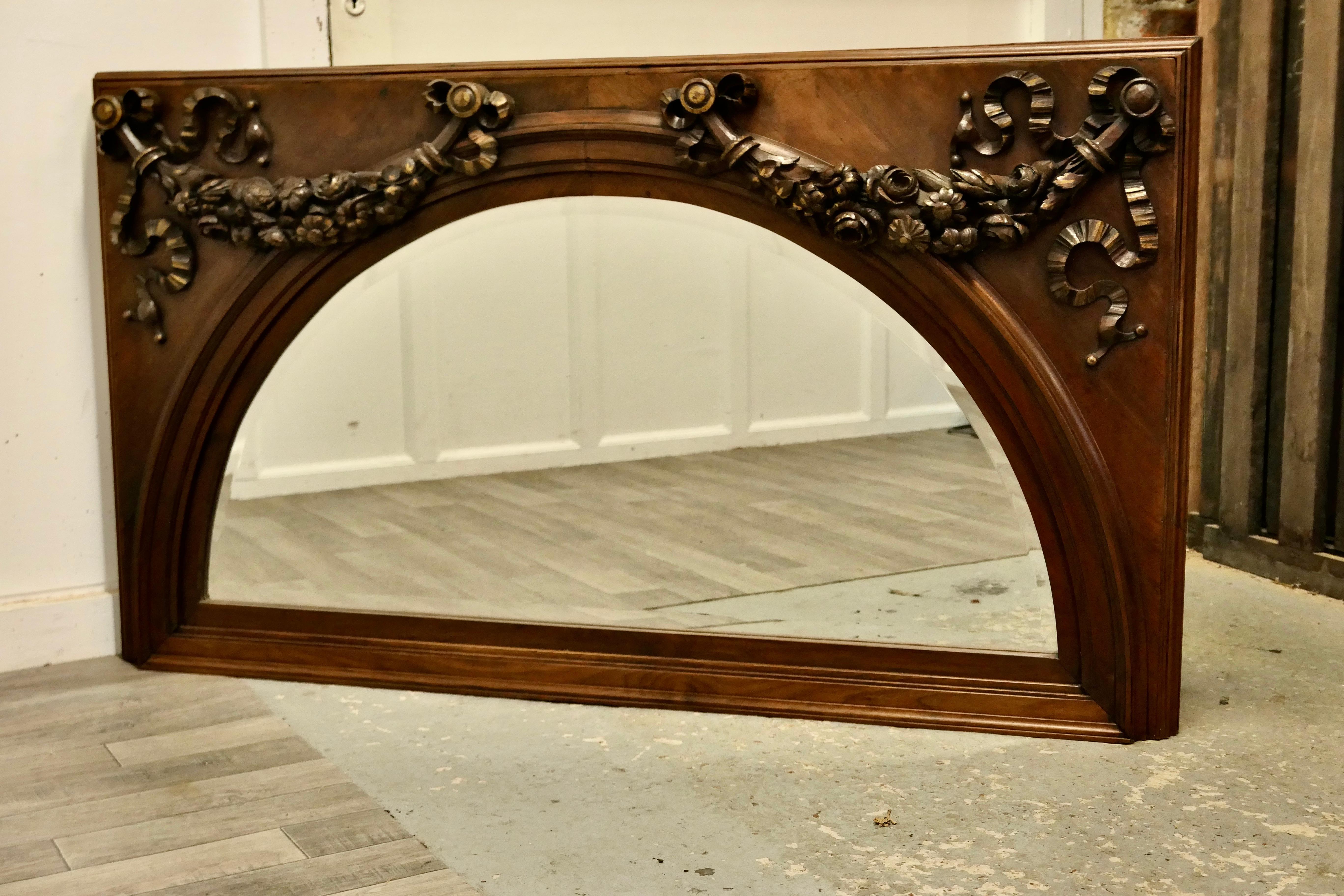 A Superb Large Carved Walnut Over mantel Mirror
This is a very Striking piece it has a rectangular shape set with an arched beveled mirror, there are deeply carved swags with garlands of flowers and ribbons decorating the top corners
The mirror has
