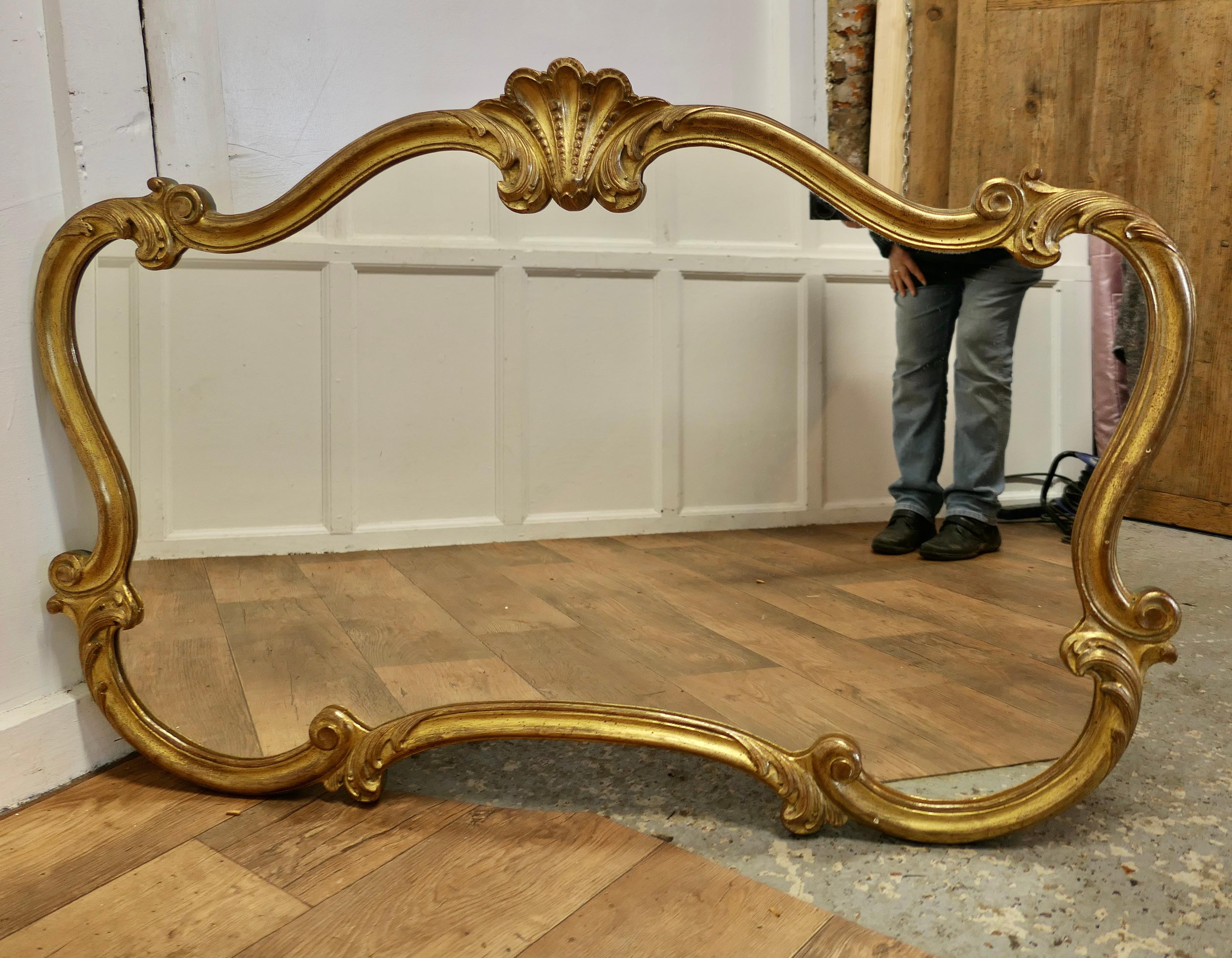 A Superb Large French Gilt Scallop Shaped Overmantel  

This is a Striking piece it has a scroll shape with curved corners there is a carved shell decoration at the top with entwined leaves around the border, which has green/blue edge
The mirror is