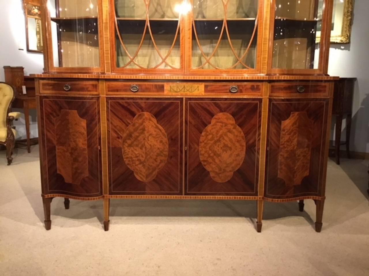 A superb quality large mahogany Edwardian Period antique display cabinet by Maple & Co of London. The upper section having serpentine ends and with a dentil inlaid cornice above a flame mahogany frieze and with a central marquetry inlaid panel. The