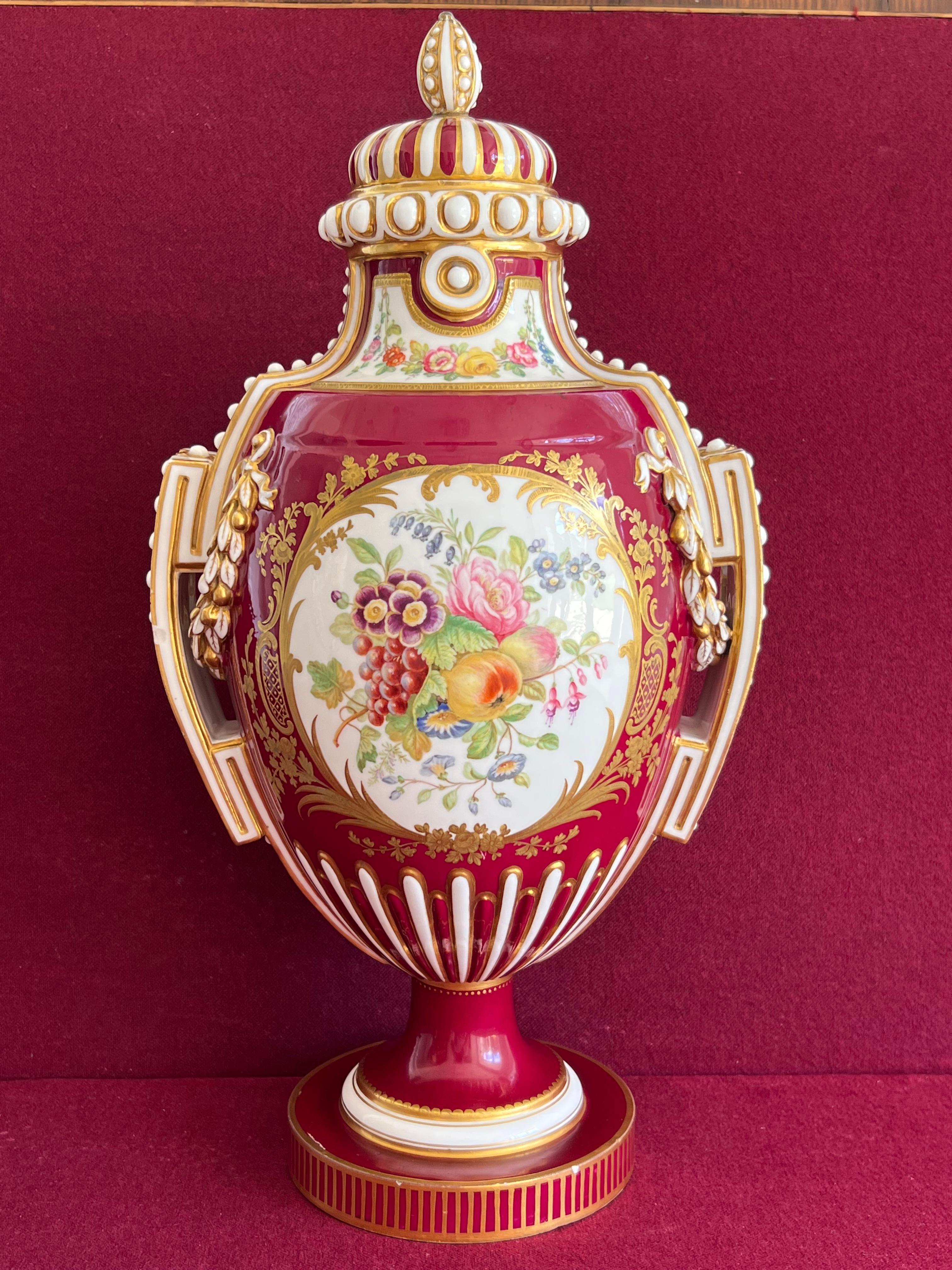 A superb pair of Coalport porcelain vases c.1850. Of urn shape with beaded handles, rims and covers picked out in gold, verily finely decorated to both sides with scrollwork panels containing fruit and flowers by William Cook, moulded laurel swags