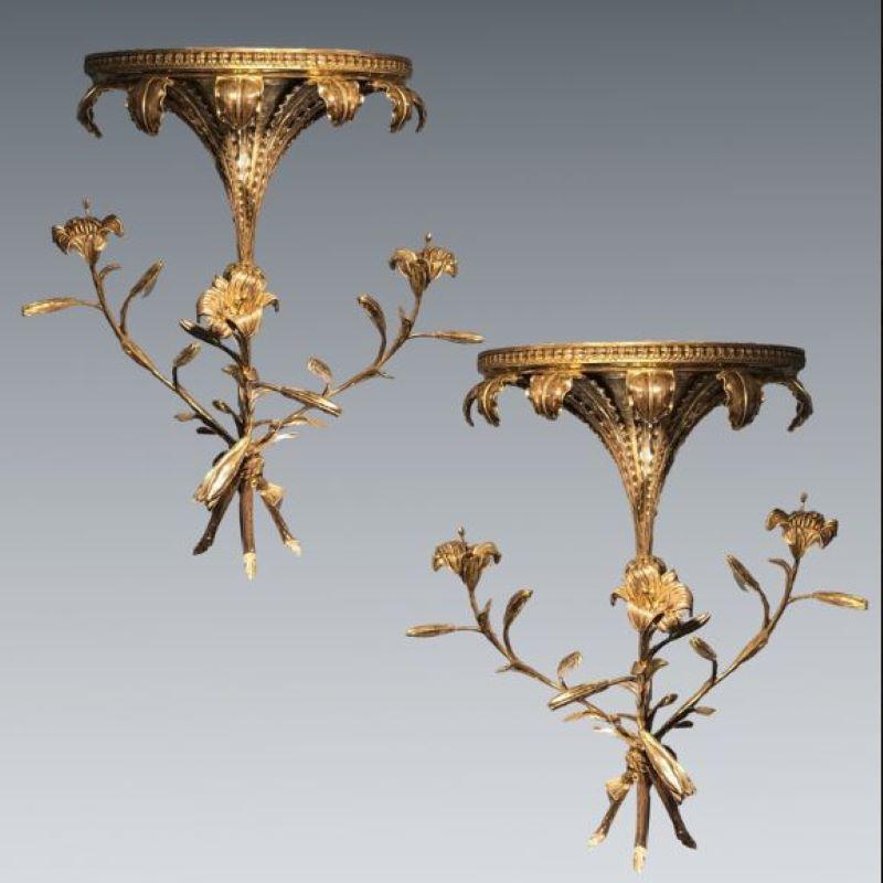 Une belle et élégante paire de consoles murales en bois doré sculpté de style Regency. Les tiges de chaque trio sont délicatement sculptées de fleurs de lys, d'étamines, de bourgeons et de feuilles, les tiges de lys étant attachées à la base par un