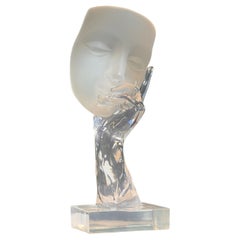 A surrealist glass and lucite sculpture of a hand holding a face, circa 1975
