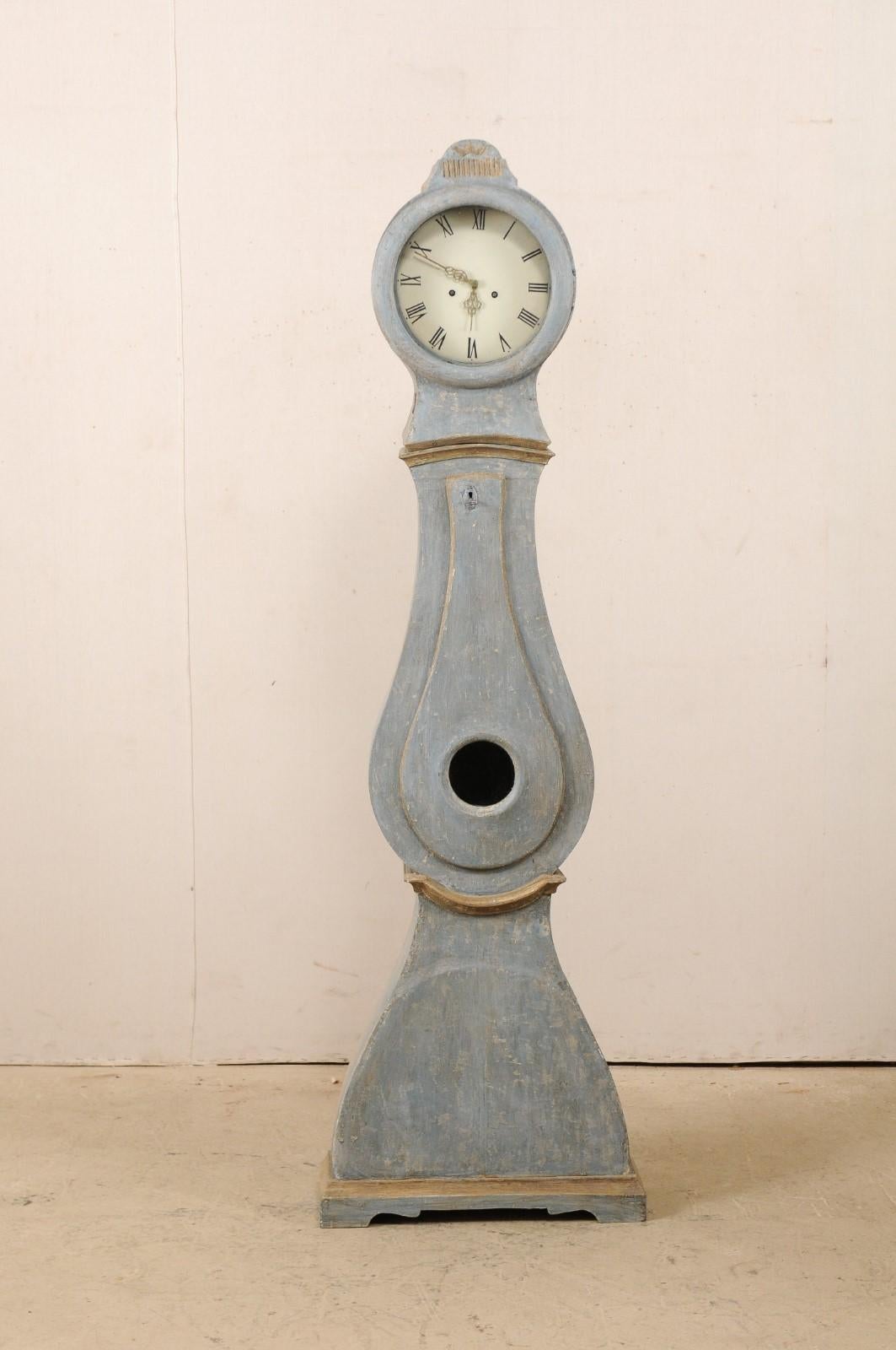 A Swedish painted wood grandfather clock from the 19th century. This antique floor clock from central Sweden features a sweetly raised arch-shaped bonnet adorned with petite carved foliage above a reed-carved banding, with its original metal face