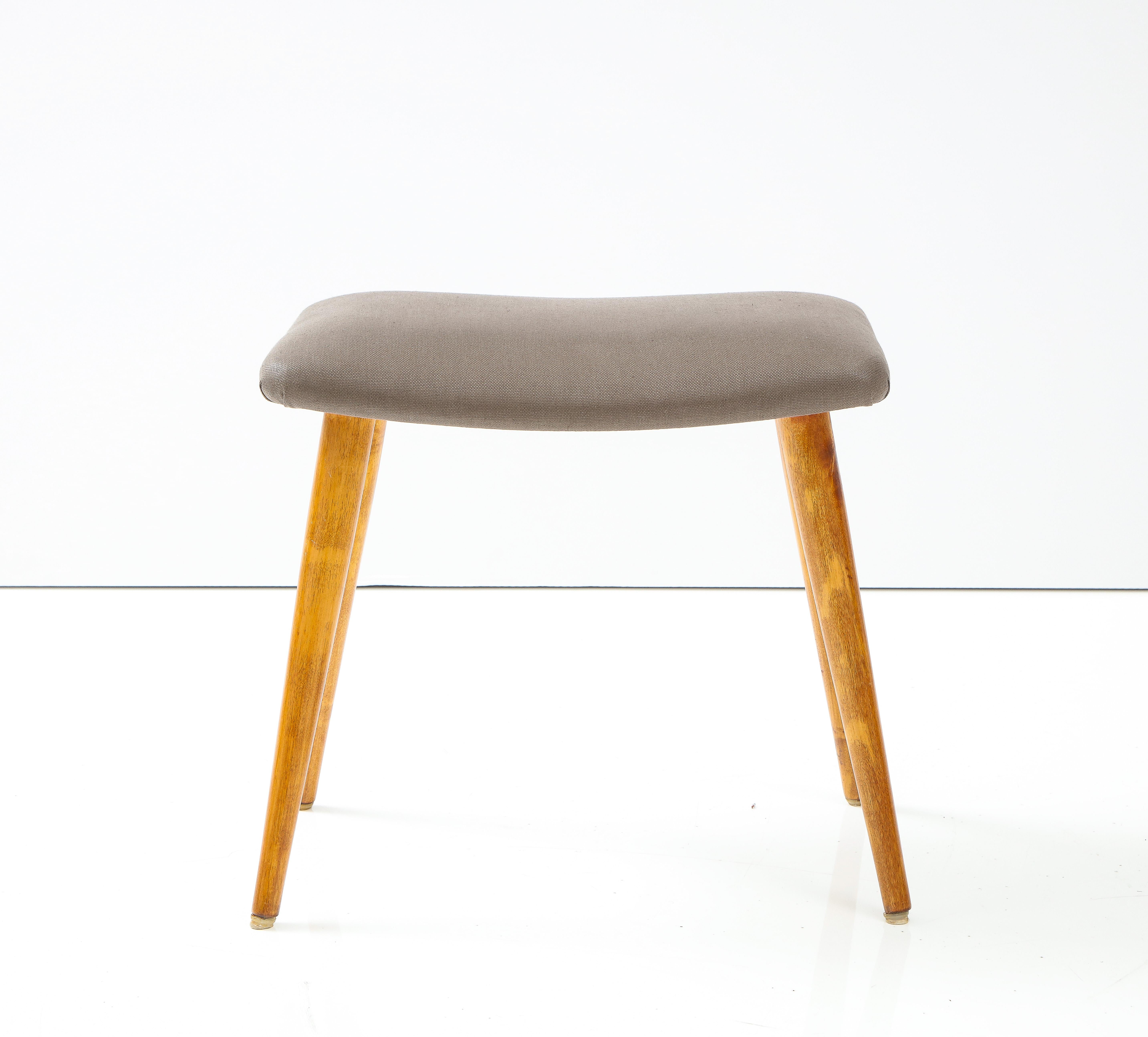 A Swedish polished birchwood stool, circa 1940s, with a rectangular glazed linen seat raised on turned and tapered legs.