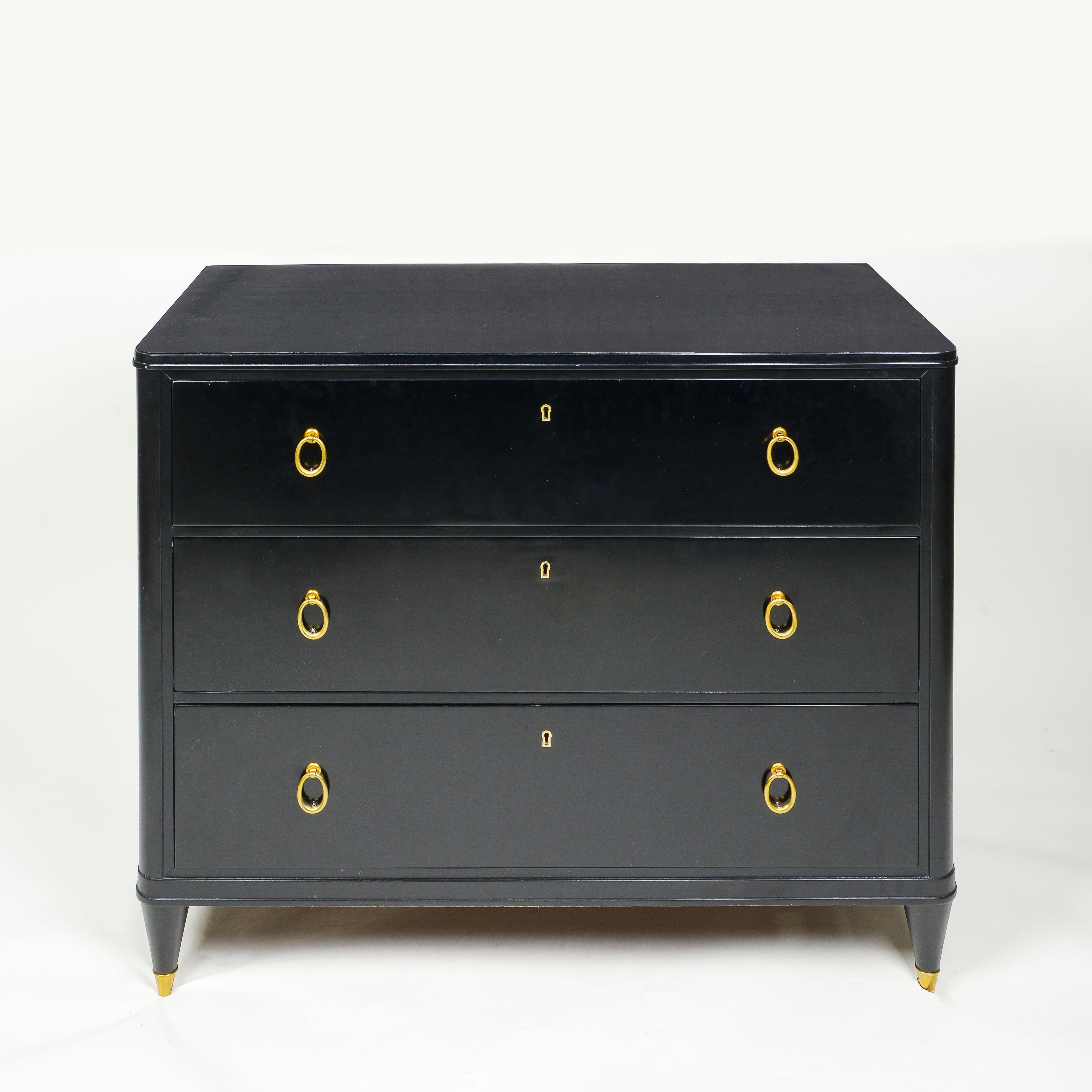Fitted with three drawers on four tapered brass feet. Each drawer features a brass-outlined escutcheon and ring pulls. Bearing Nordiska Kompaniet label.