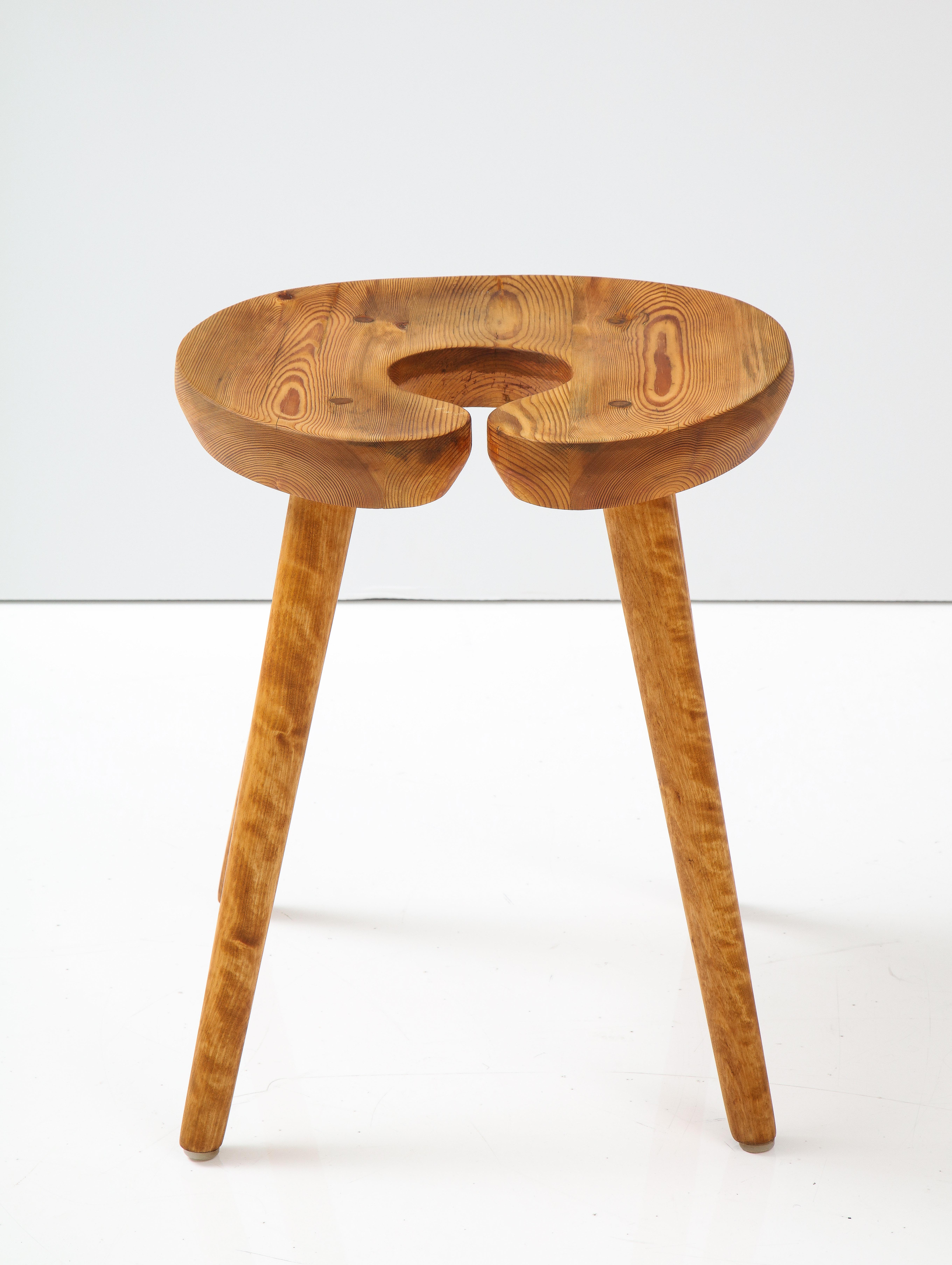 A Swedish sculptural birch and pine stool, Circa 1960s, with a carved C-form seat raised on turned birch legs. 