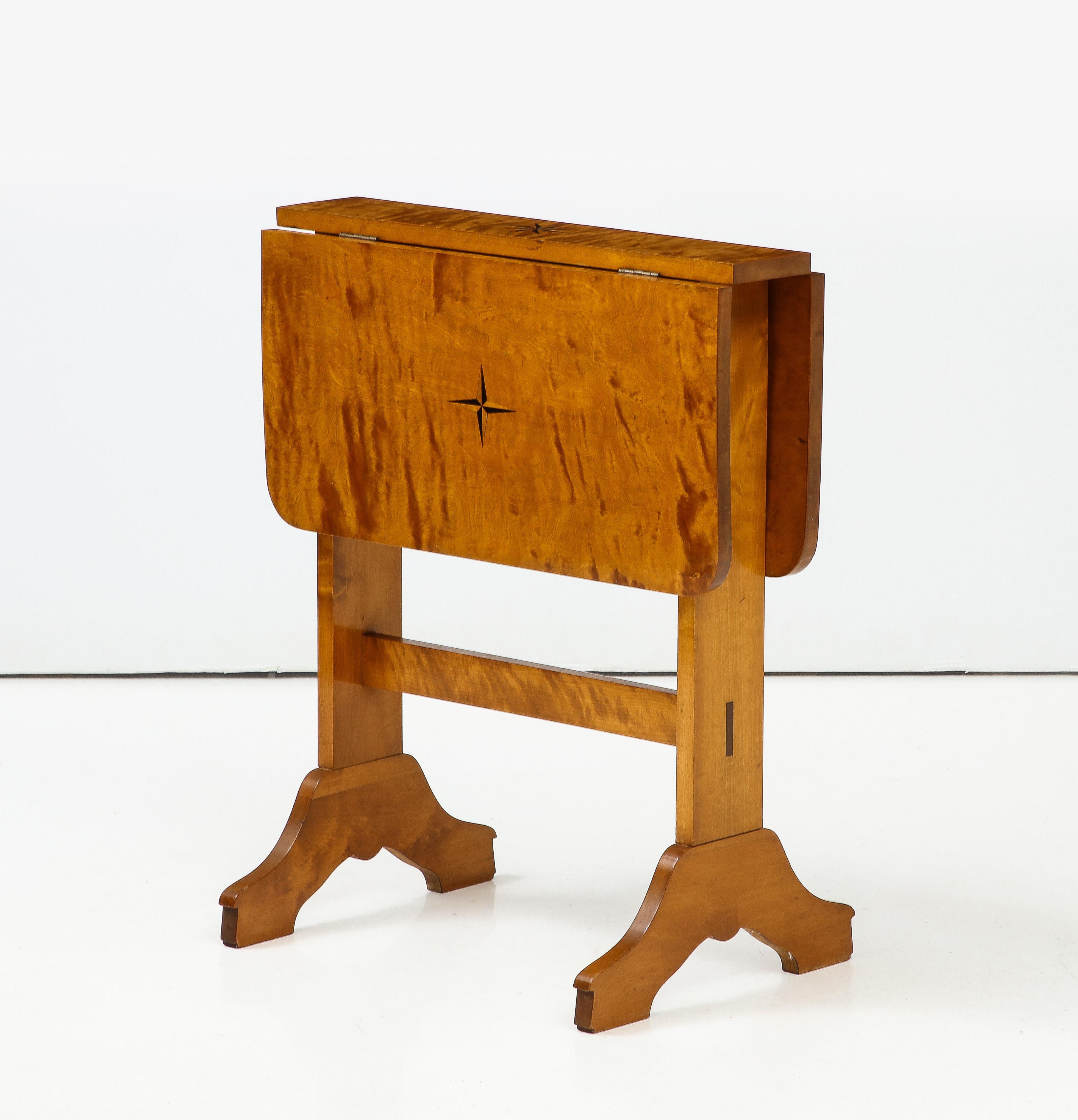 Schwedischer Deko-Tisch mit Intarsien aus Birkenholz, ca. 1930er Jahre, rechteckige Tischplatte mit 2 Fallblättern, durch Schwenken der Tischplatte erhöht.  Stützen mit einer Querstrebe und nach unten gebogenen Füßen. 
25,25 Zoll - Breite mit