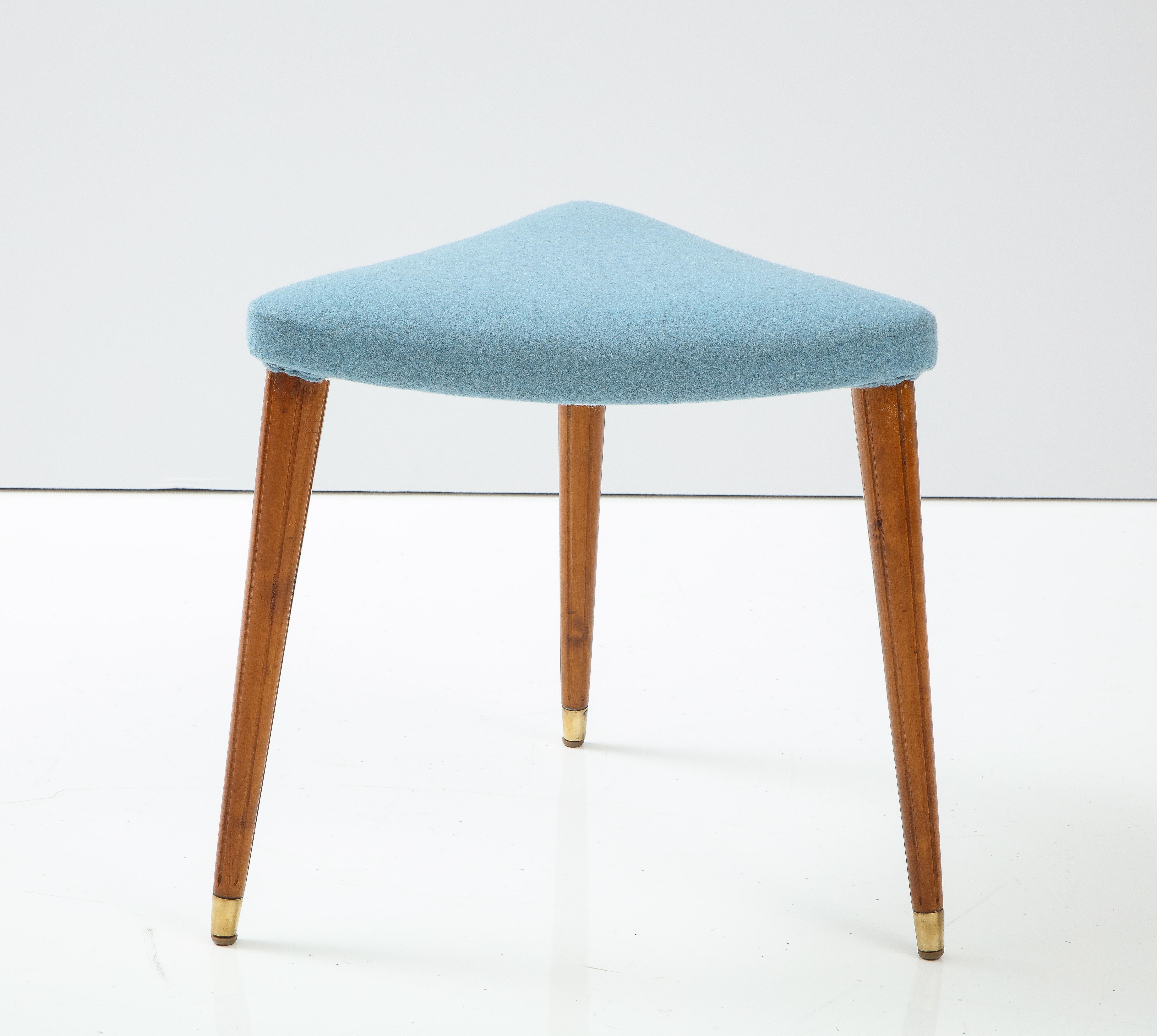 A Swedish Grace birchwood and upholstered stool, Circa 1940s, the upholstered triangular top raised on three turned tapered legs with fluting and ending with brass sabots.


