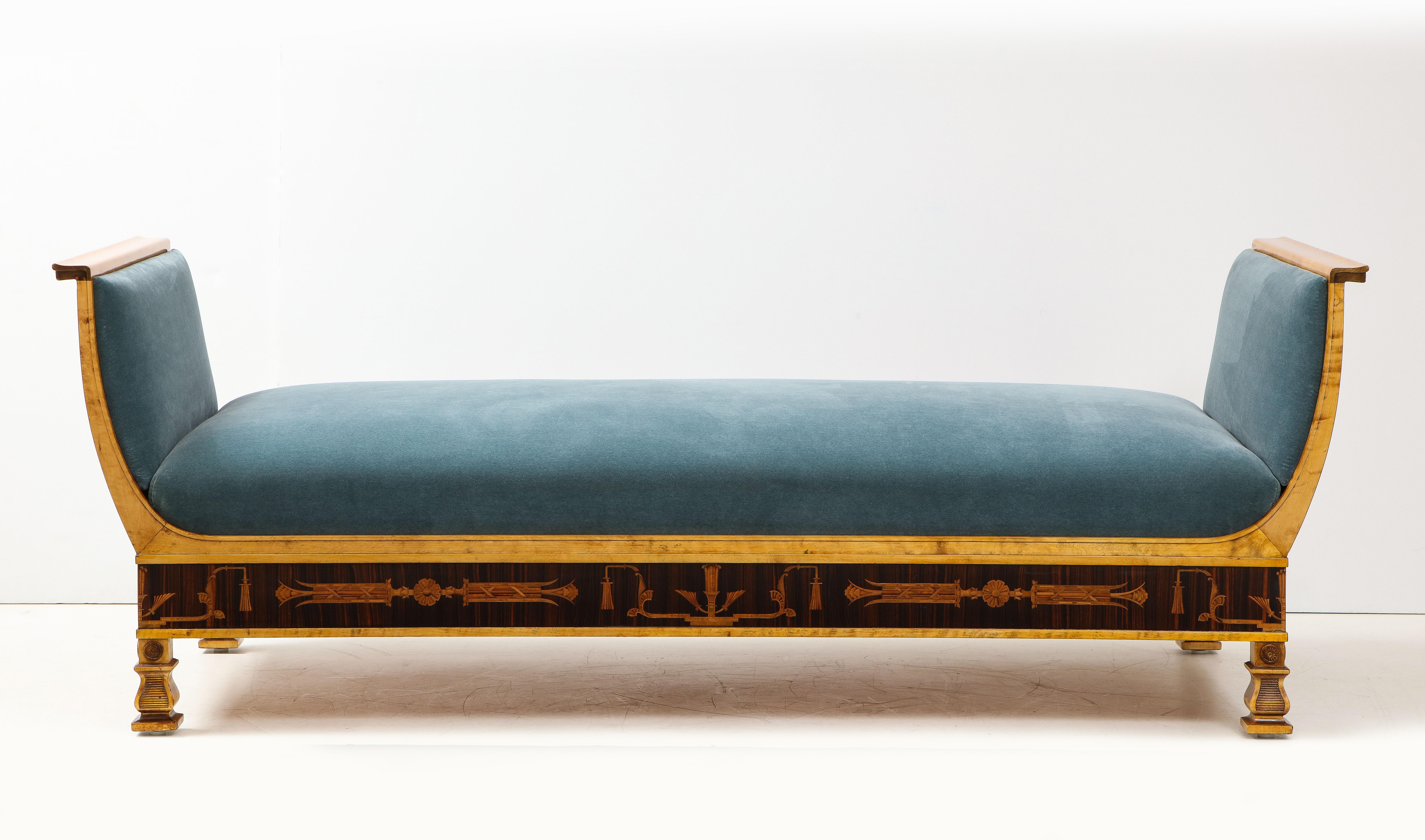 A Swedish Grace birchwood and jacaranda inlaid daybed, Circa 1920-1930, designed by Carl Malmsten and produced by Svenska Möbelfabrikerna Bodafors, with new velvet upholstery between out curved sides, an inlaid stylized classical frieze raised on