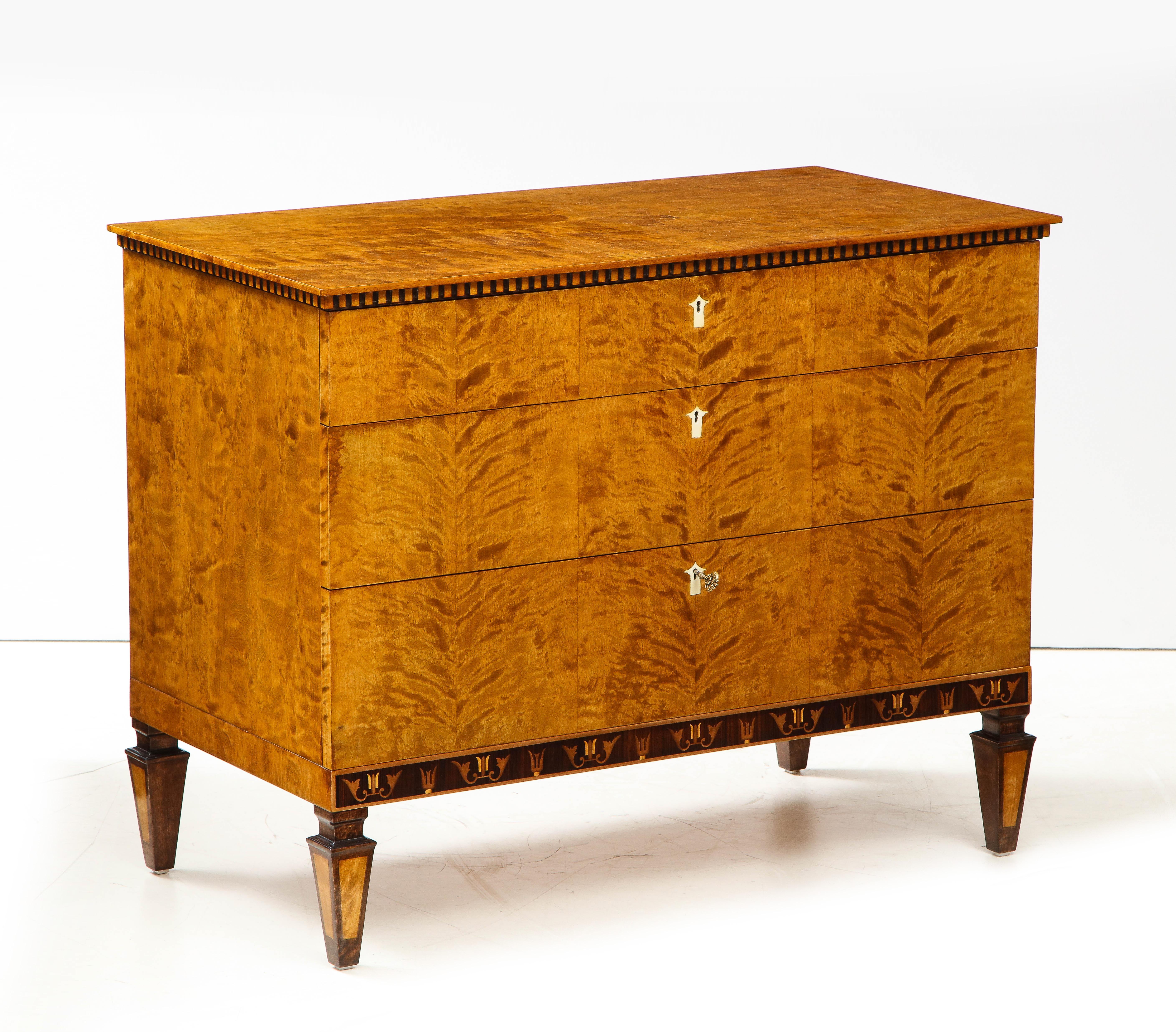 A Swedish Grace flamed birch wood and palisander inlaid chest of drawers, Circa 1920-1930, the rectangular top above a dentil molded frieze and three long drawers, the lower frieze with Classic Swedish Deco inlays raised on square tapered feet.