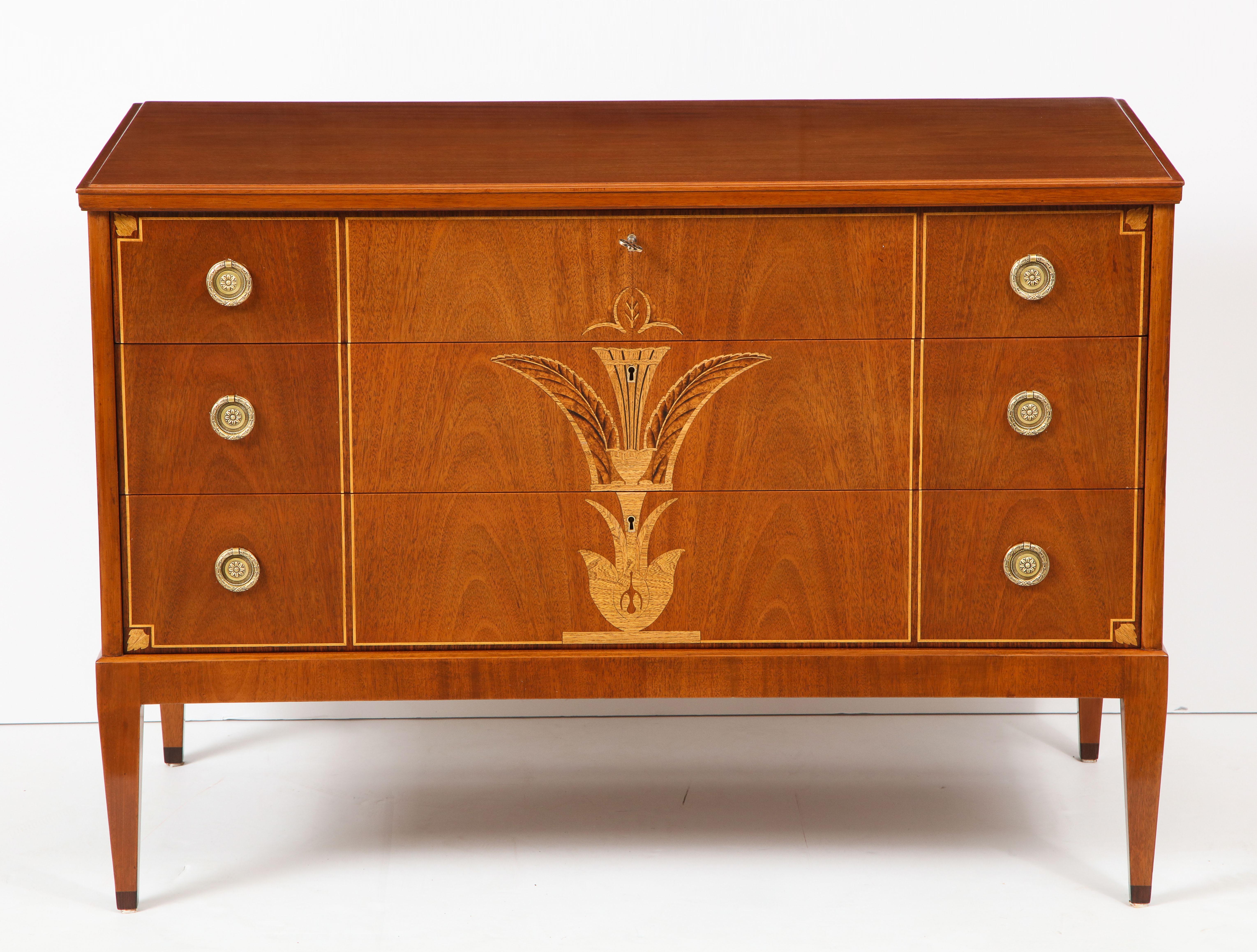 A Swedish Grace fruitwood & birchwood inlaid light mahogany commode, circa 1930s, for Nordiska Kompaniet, with a rectangular top above three flush fitting long drawers raised on square tapered legs. Metal retailers label on verso.