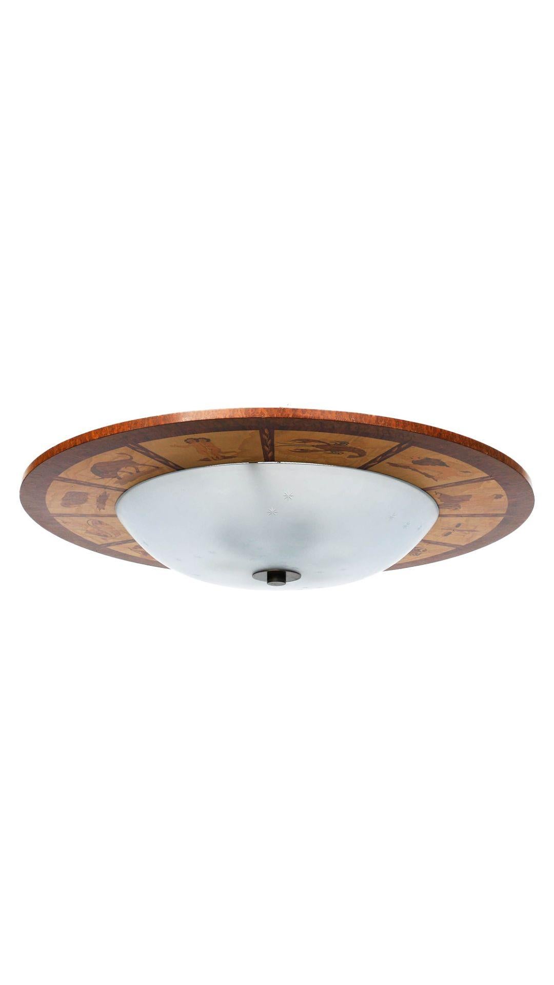 A Swedish Grace-period marquetry flush mount with stylized depictions of the twelve Zodiac signs. The round domed glass diffuser with cut glass stars, complimenting the astrological theme of the fixture. Circa 1930, signed Mjölby Intarsia. Price