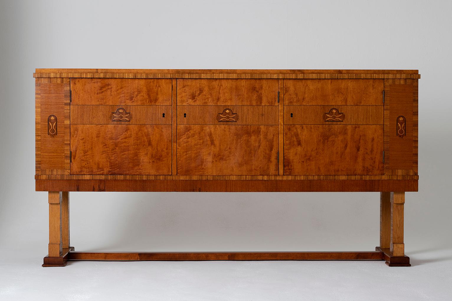 A Swedish Grace birch and Zebrano three-door sideboard,
Each door with a marquetry motif and internally veneered with birch, revealing a central shelf, resting on a geometric neoclassical base, flanked by side doors (one of which fitted with green