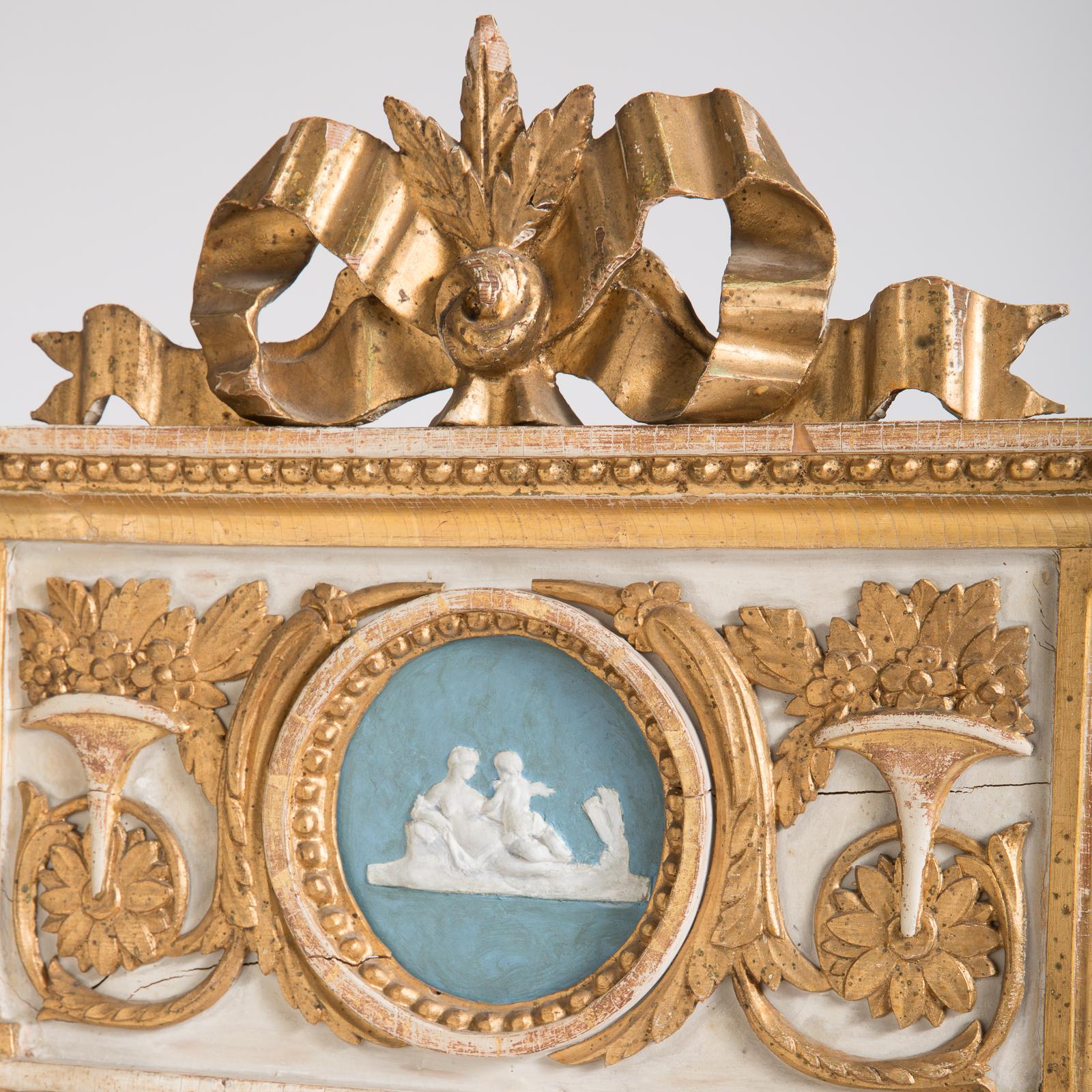 This elegant mirror from the Gustavian period has the old divided glass and gilt ornamentation of flowers in a trumpet vase on a white ground topped with a gilt bow. The bottom panel shows a row of carved pineapples. The center medallion on a blue