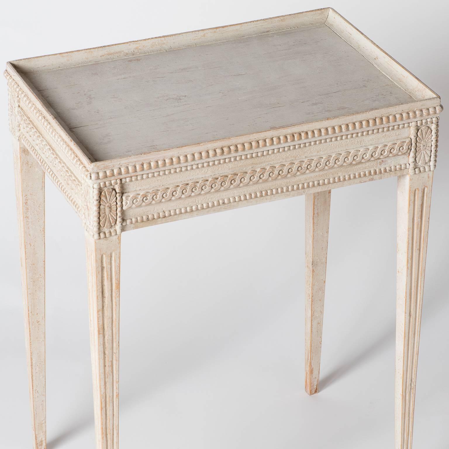 This elegant Gustavian style table has an intricate decorative design on the apron and ends in tapered reeded legs. The pale off-white paint surface is original.

Measures: 29” high
22” wide
14.75” deep.