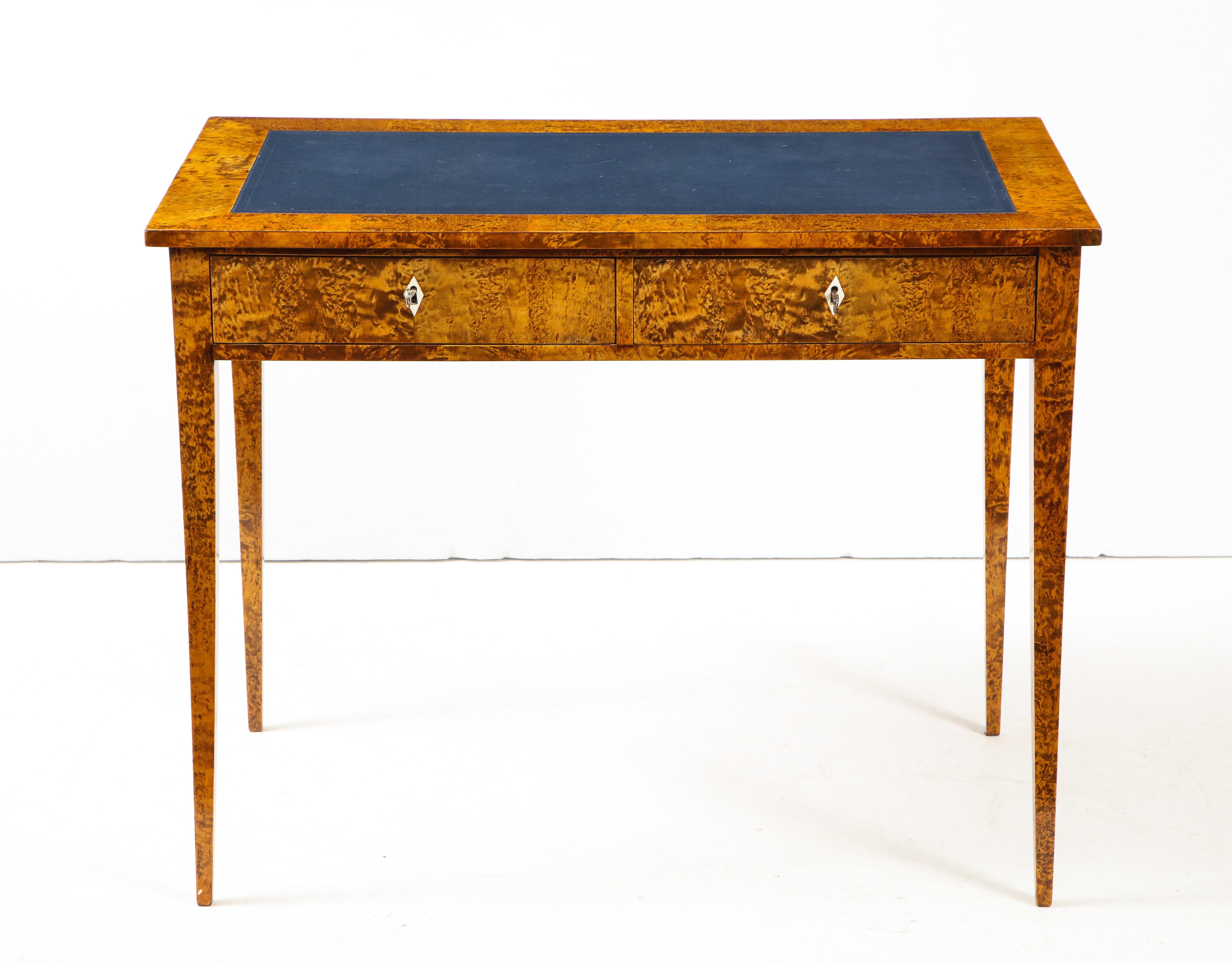 A Swedish Karelian birch writing table, second half of the 19th century, the dark blue inset leather writing surface surrounded by a rectangular border, two frieze drawers raised on elegant square tapered legs. Super example of figured Karelian