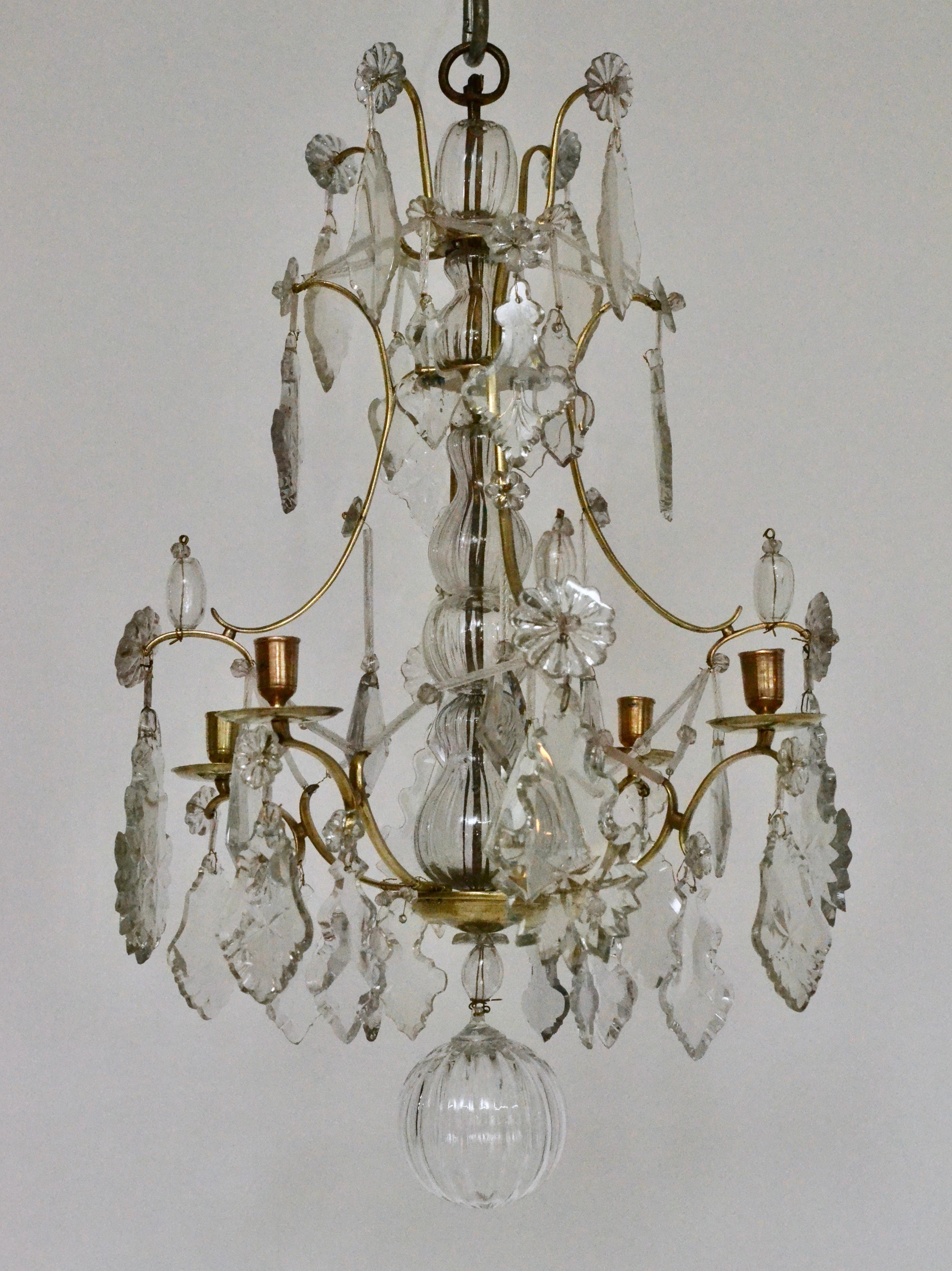 A small Swedish Louis XV polished brass and cut-glass four-light chandelier, 18th century.
The brass cage hung with cut-glass leaf-shaped pendants and other shapes. The center stem dressed with blown glass pieces ending below with a blown glass