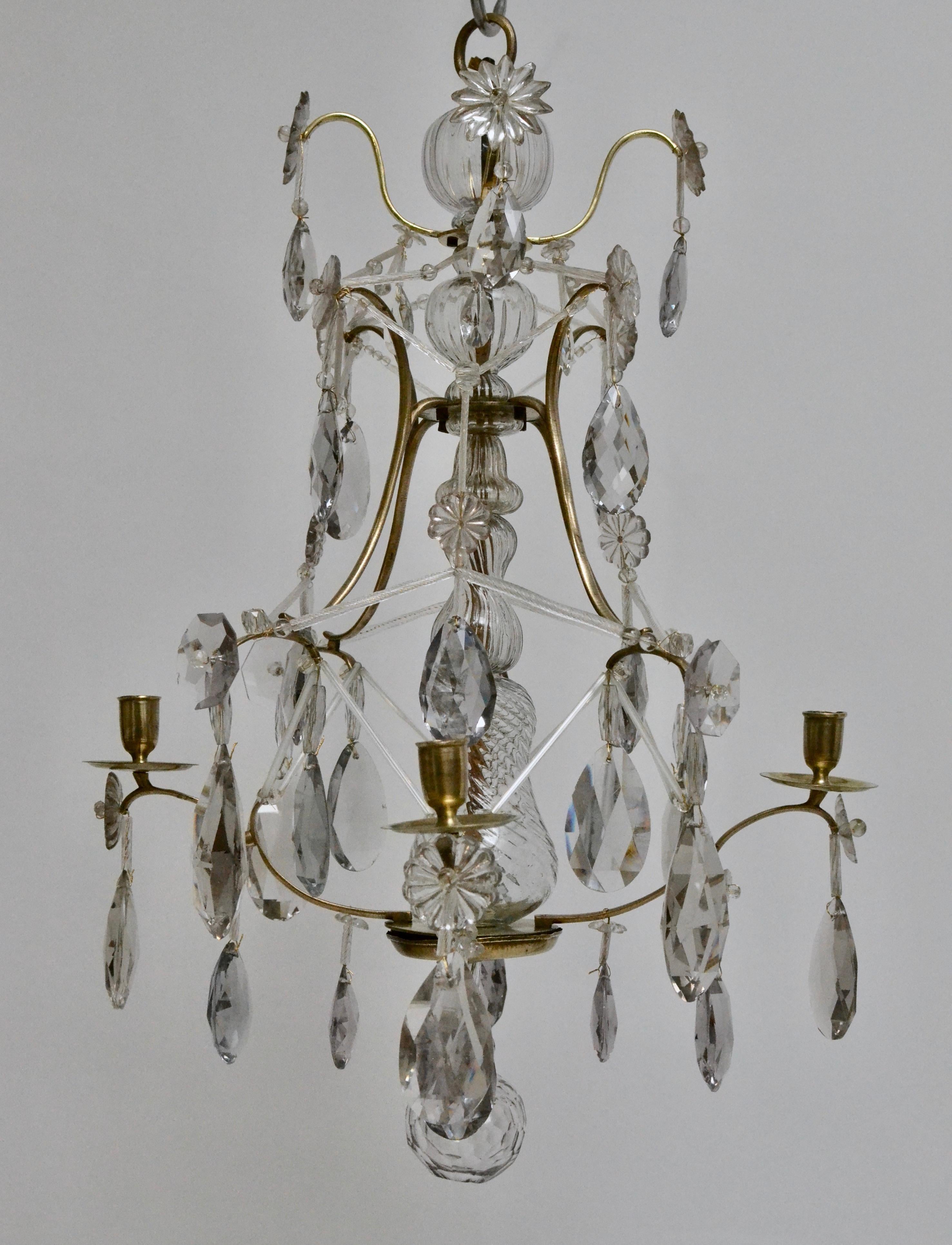 A small Swedish Louis XVI polished brass and cut-glass four-light chandelier, 18th century. The brass cage hung with cut-glass pendants and other shapes. The center stem dressed with blown glass pieces ending below with a cut-glass boll. The small