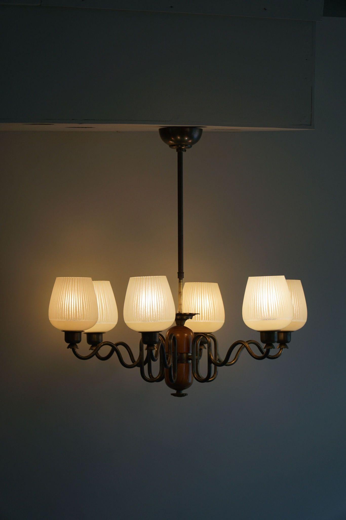 Questo elegante lampadario Swedish Modern degli anni '40 esemplifica l'estetica Art Deco con il suo design sofisticato. Presenta sei bracci in ottone graziosamente curvi, ognuno dei quali sostiene un paralume in vetro a strisce che aggiunge un tocco