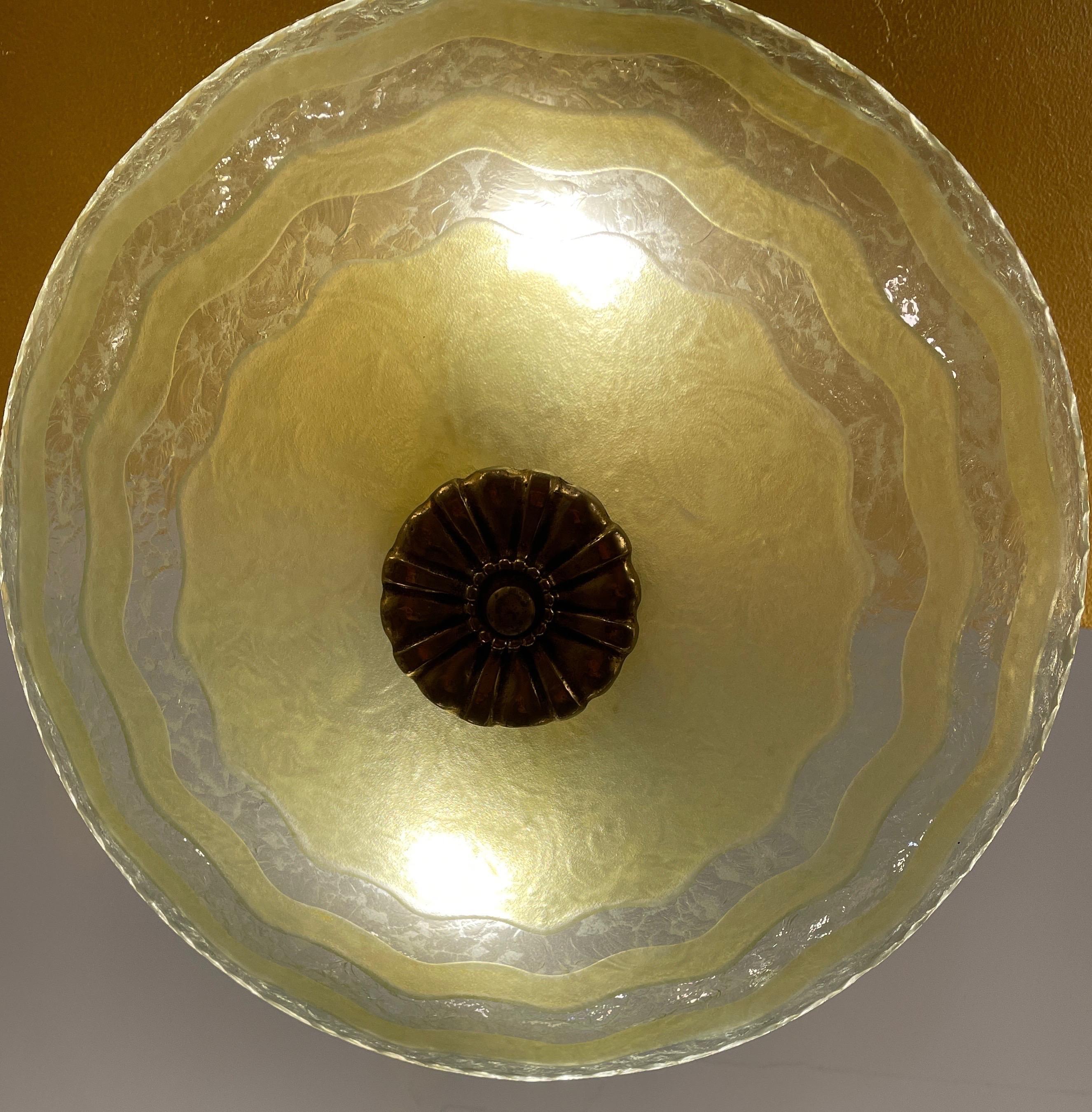 This lovely fixture relies on molded textured glass on the interior surface and wavy carving and a stain on the exterior surface to create the happy, stylized floral pattern. A brass medallion affixes the hardware to the glass. Currently rewired to
