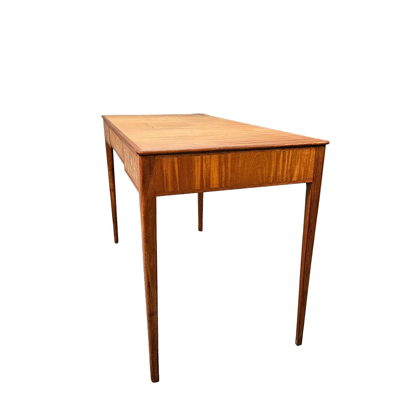 A refined Swedish writing table by the firm of designer Ferdinand Lundquist. Featuring three drawers with detailed marquetry inlays of trailing leaves and flowers. The front showcases delicate intarsia work in a variety of light woods, set against a