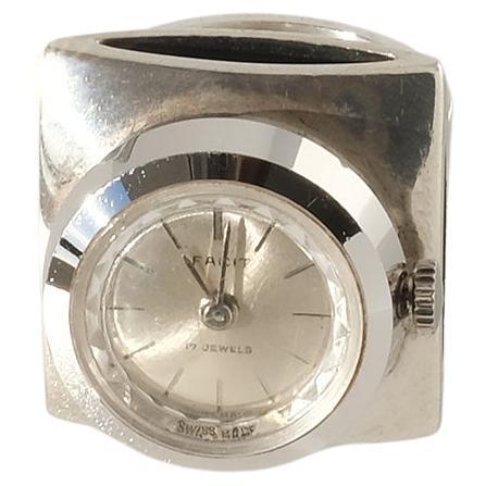 This silver ring has a watch on top. The watch has a mechanic clockwork. Its case is round with a pearl-colored dial which is embraced by a shimmering frame. You set the time by pulling out and turning the crown.

This ring is, in our opinion, a