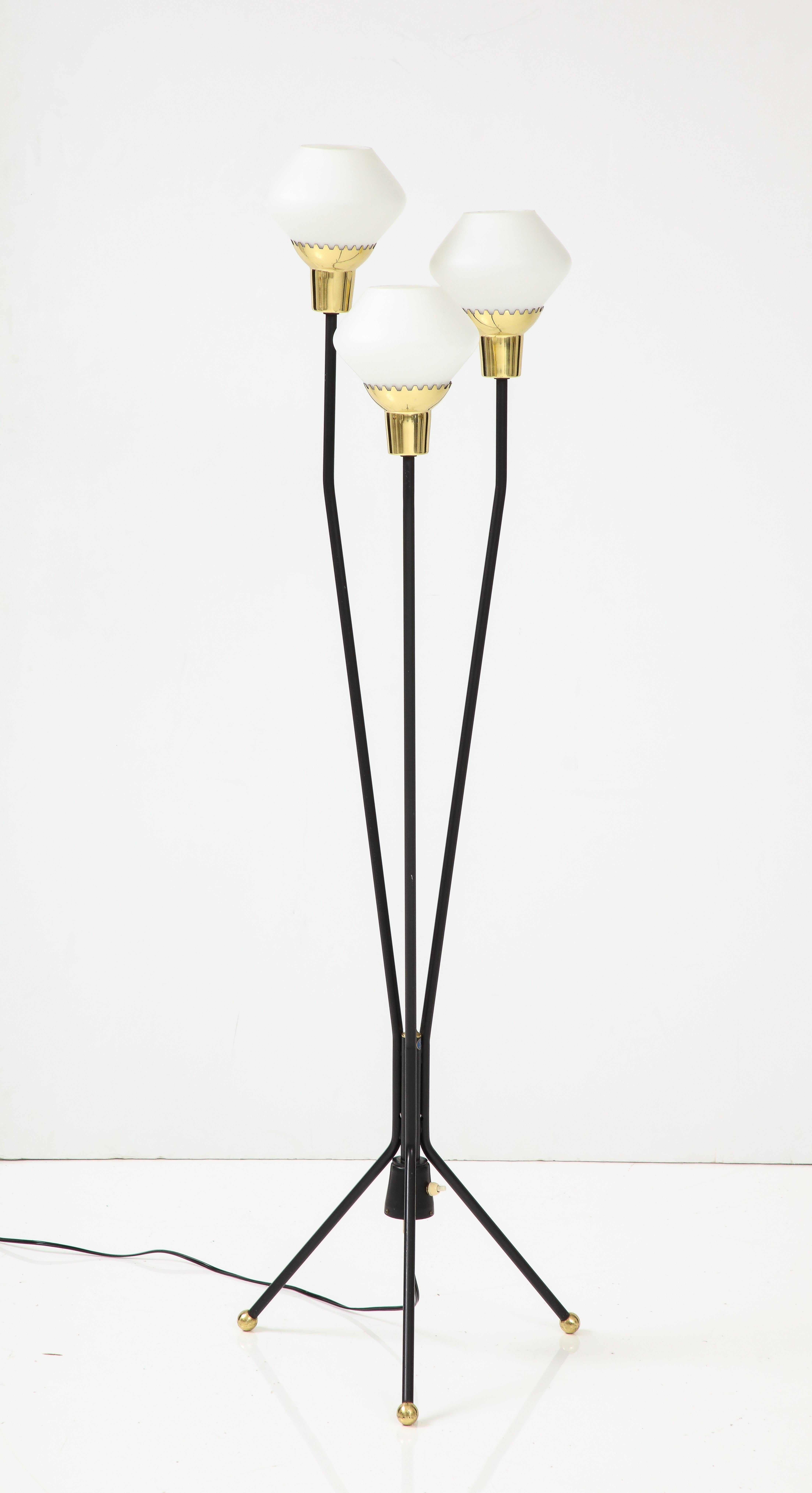 A Swedish black painted metal three branch floor lamp, circa 1940, with a tripod base ending with brass ball feet, the white glass shades supported by brass crown brackets.
Swedish stamp on base. 3 x 60w max. Re-wired for US.