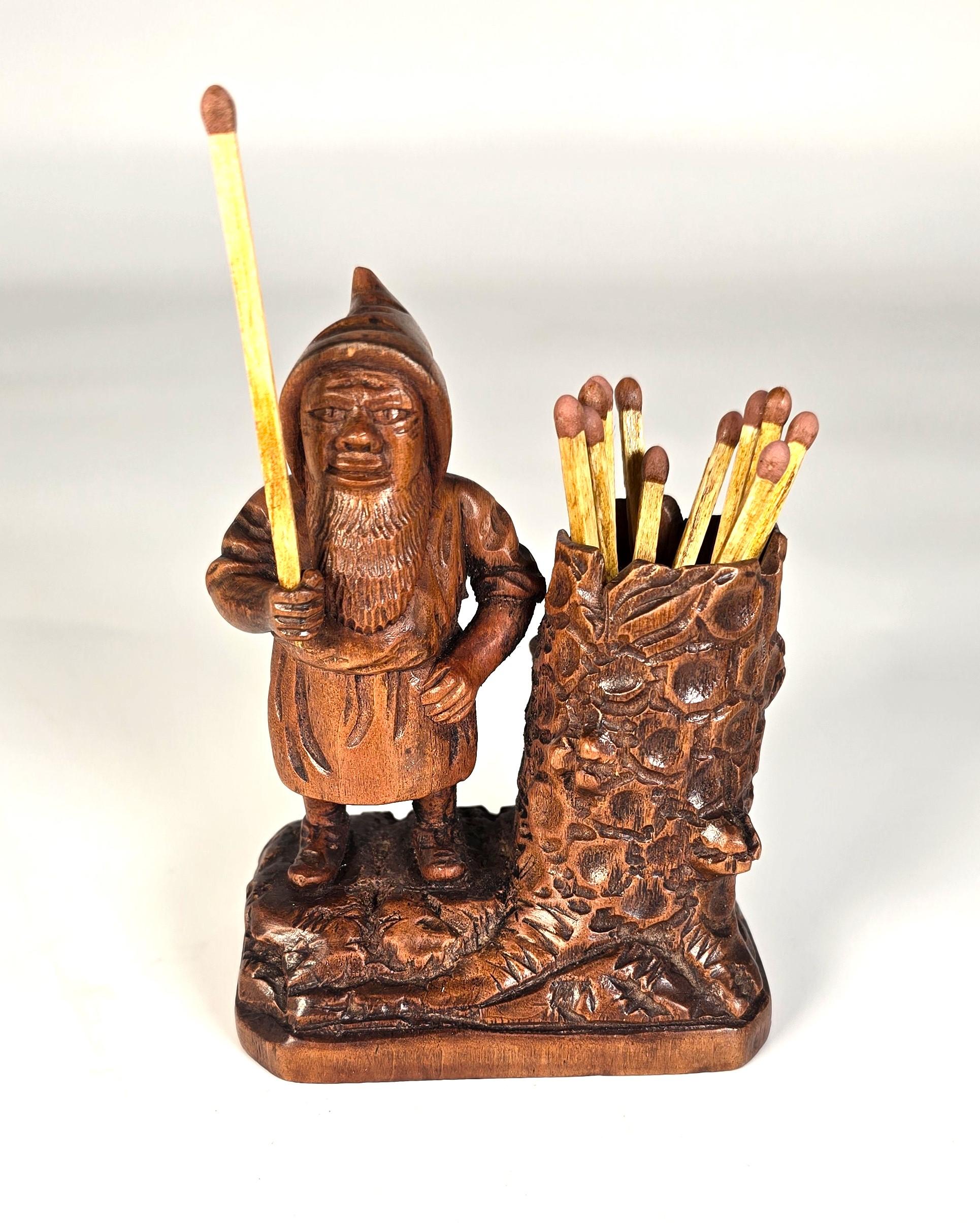 Ce superbe petit porte-allumettes en bois de tilleul sculpté à la main de la Forêt-Noire représente un gnome debout portant un grand chapeau à visière, une tunique et une longue barbe.

Ce petit bonhomme se tient debout, une main levée, avec un trou