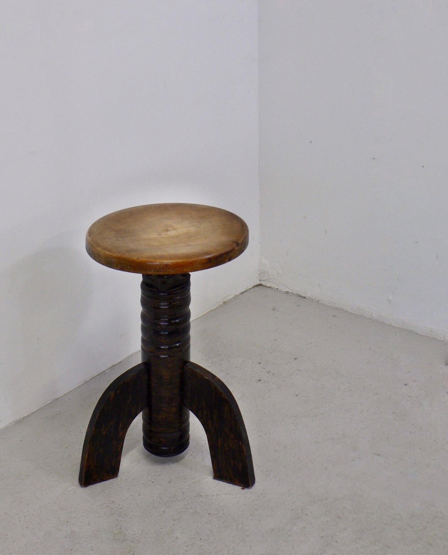 wiveling, height-adjustable, tripod stool from early 20th-century France. The tripod base is made of stained wood, and the seat is height-adjustable with a steel screw.