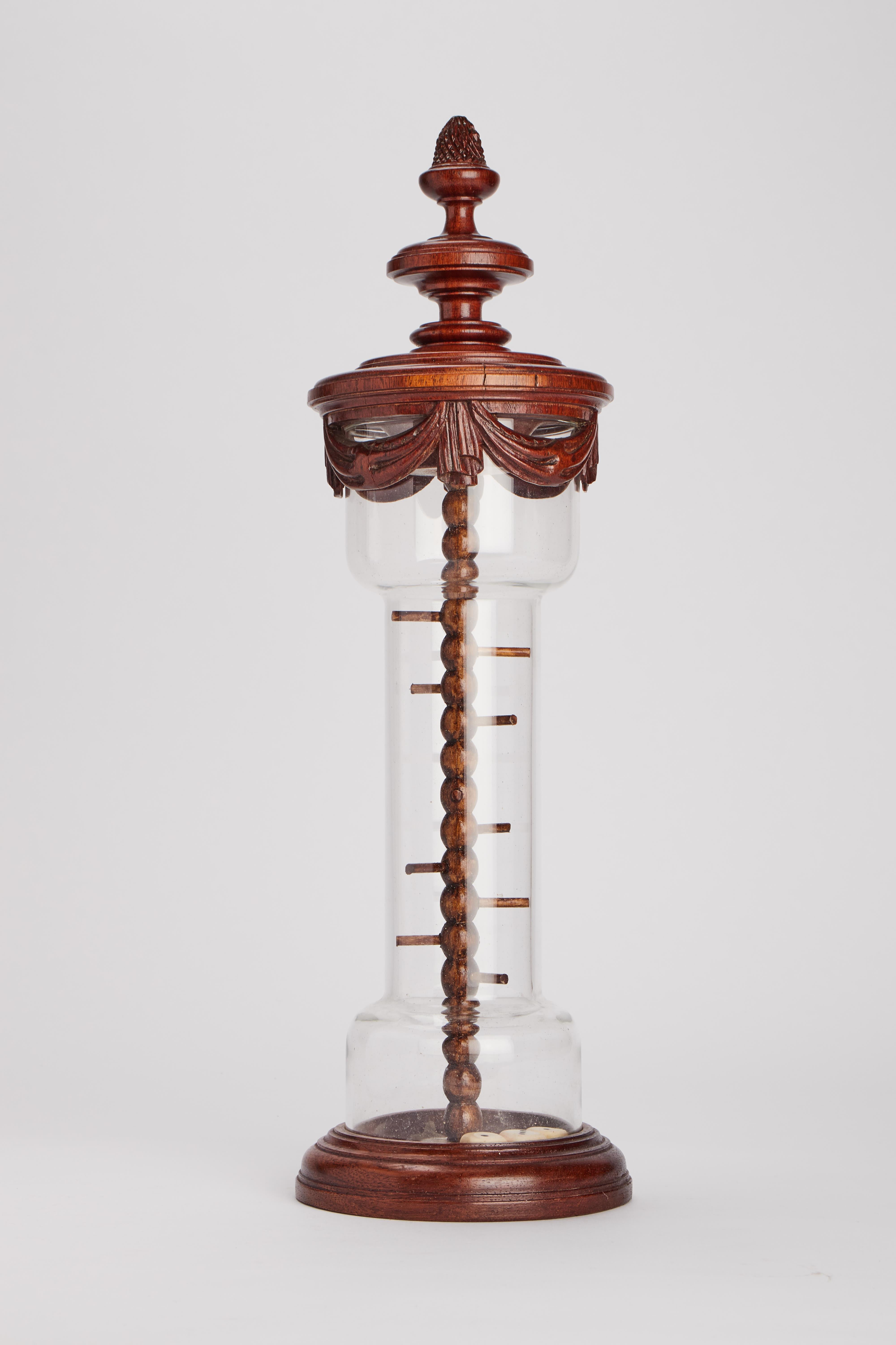 Un jeu de société avec des dés.
La base, le couvercle et l'élément central sont en bois de chêne, le cylindre est en verre et contient trois dés. France, fin du XIXe siècle.
