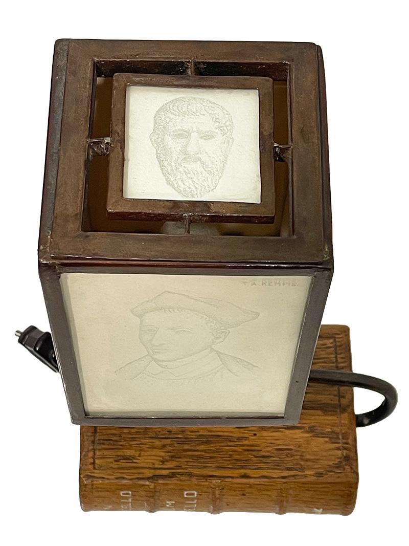 A table reading lamp with engraved glass with portraits from the 15th century

A table reading amp on a base of a book with a curved stand, on top of which is a square of glass-engraved portraits with paper in the background. The portraits are T.A.