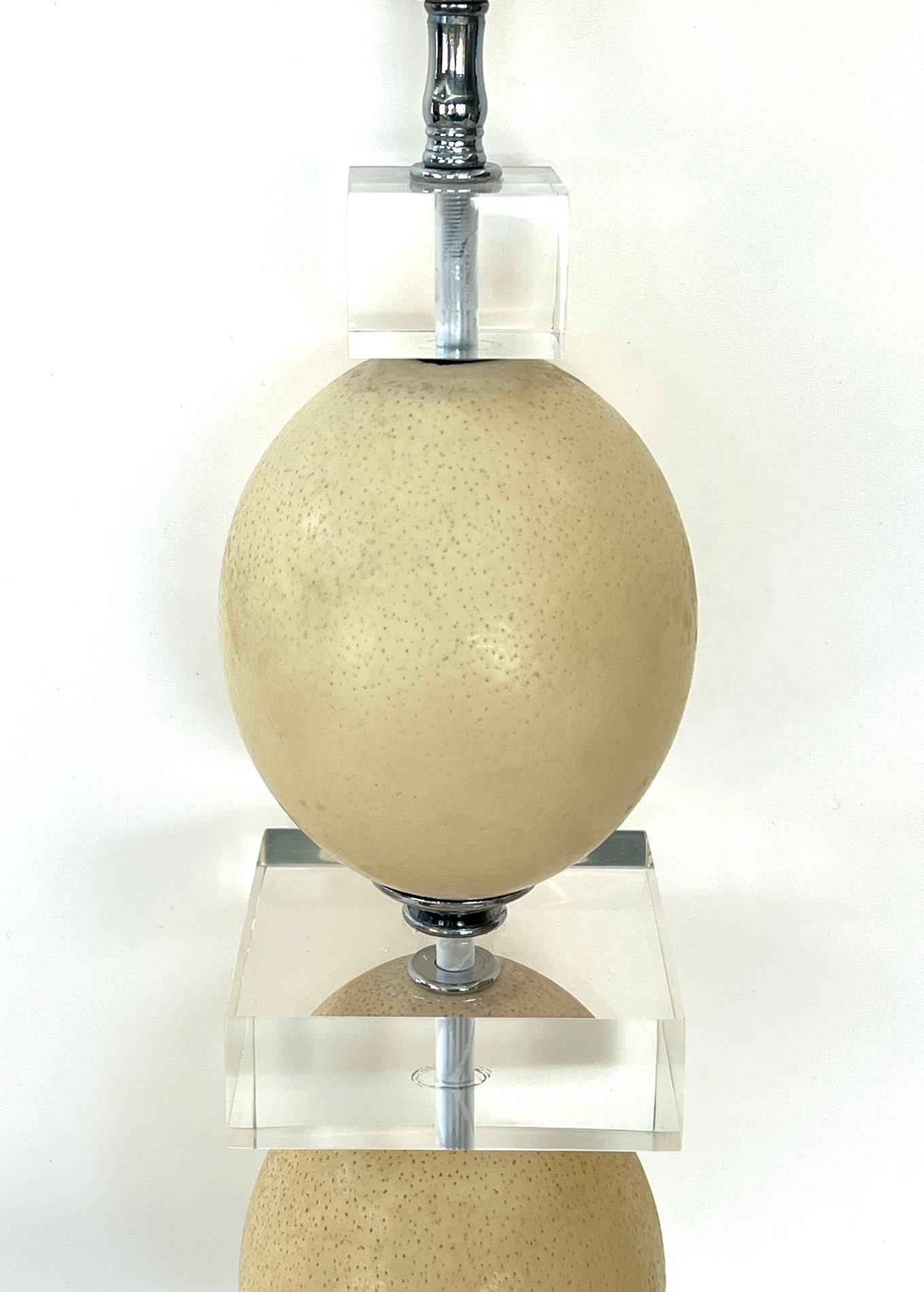 the tall lamp consisting of 2 large ceramic-like ostrich eggs divided by geometric lucite elements all over a stepped base