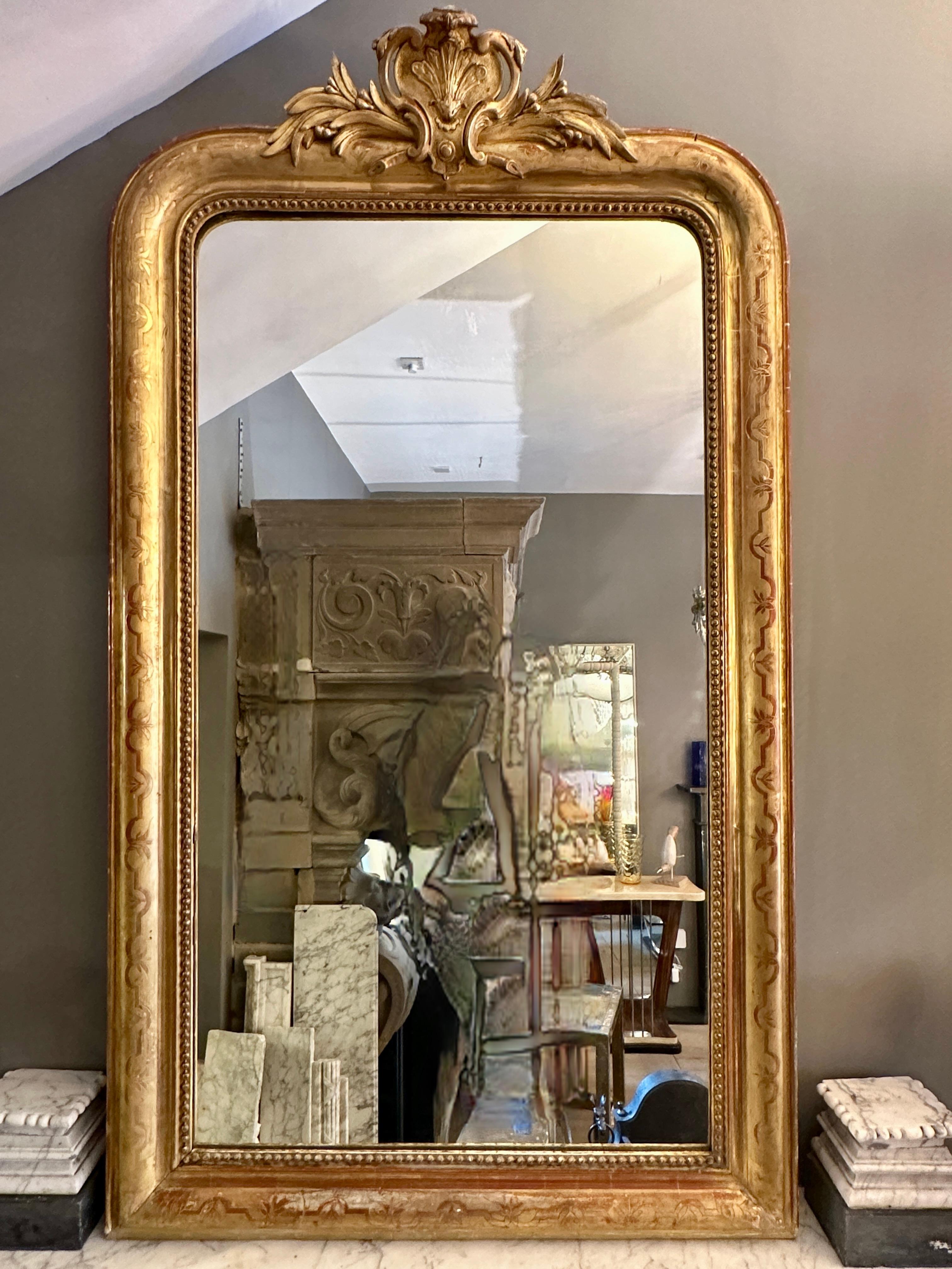 An antique 19th century French gold gilt mirror in the Louis XV manner with original mirror plate. Dated from roughly 1880, boarded back intact. The frame with classical motif and intertwined floral gilt work with a  decorative crested top, plain