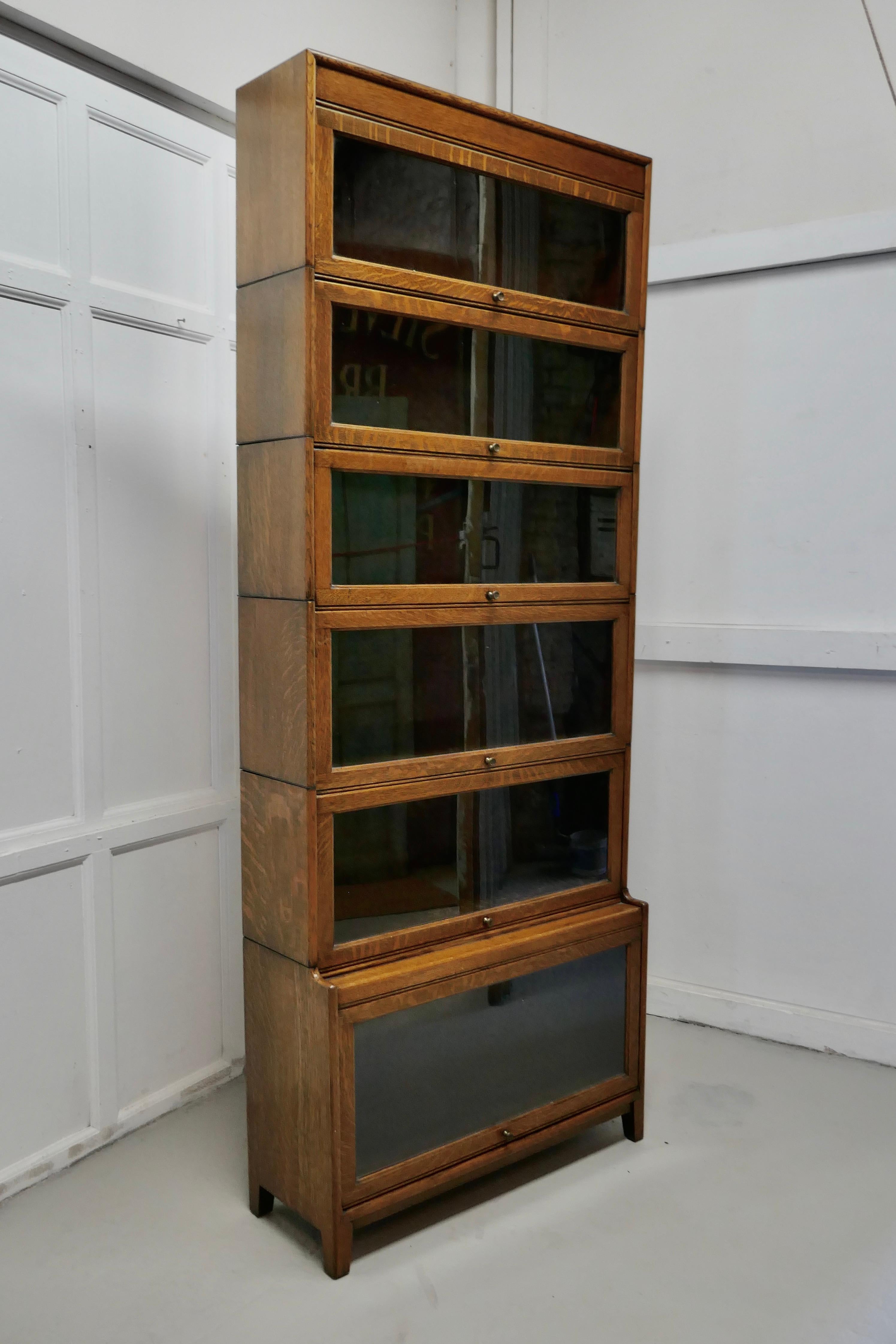 A tall Art Deco golden oak barrister waterfall bookcase, made by Gumm

The bookcase is very tall made up from 6 section all of which are stamped with the makers name “Gumm”

All the sections of the bookcase have glazed up and over doors which