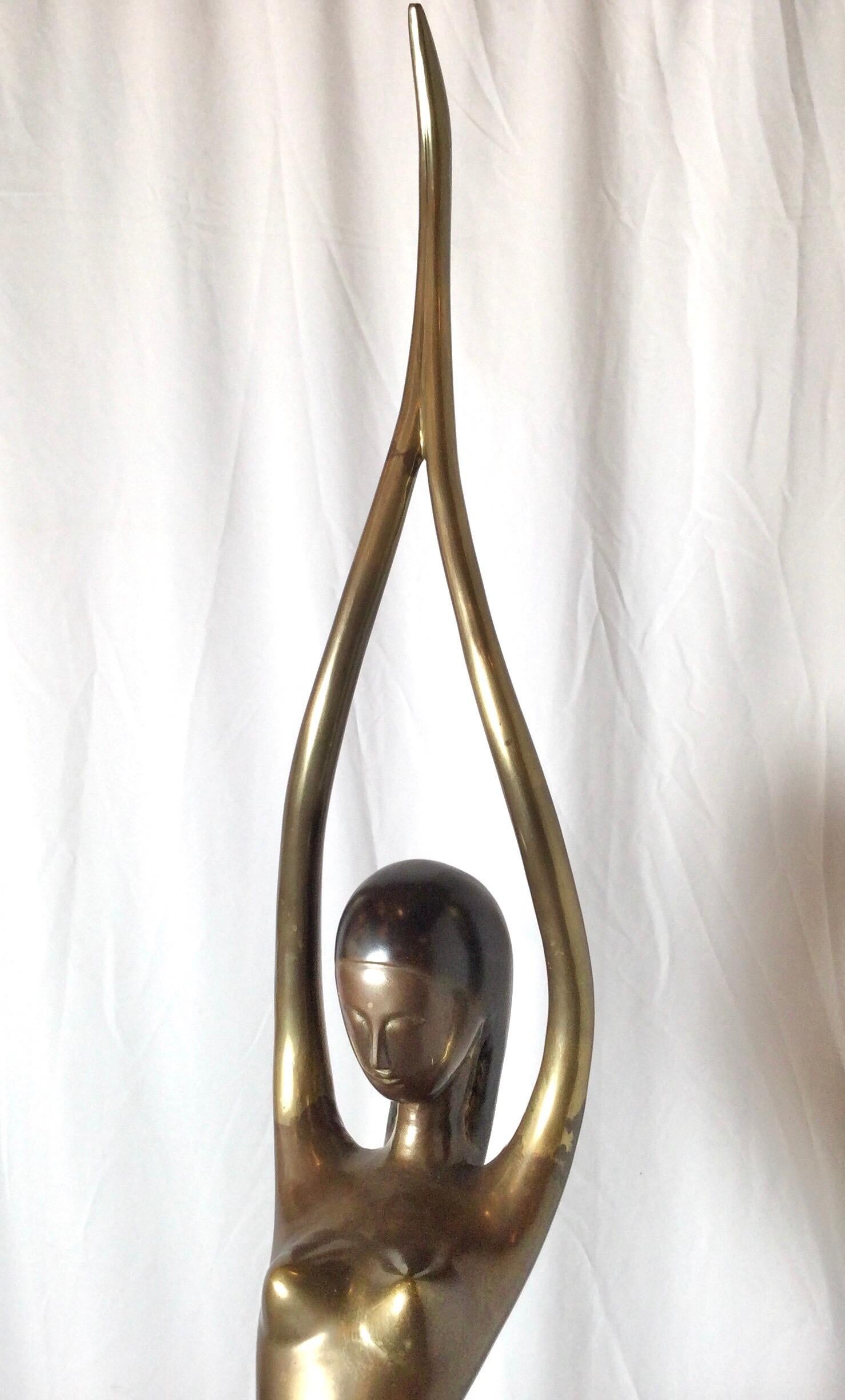 Art Deco style elongated brass sculpture of a standing woman with arms above her head.