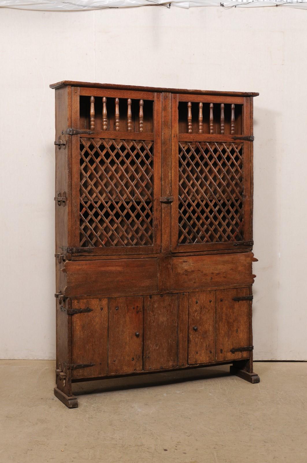 A tall Italian wooden storage and display cabinet from the early 18th century. This antique cabinet from Italy, which stands approximately 6.75 feet tall, has a flat top and upper section is fitted with a pair of wooden doors with spindle tops over