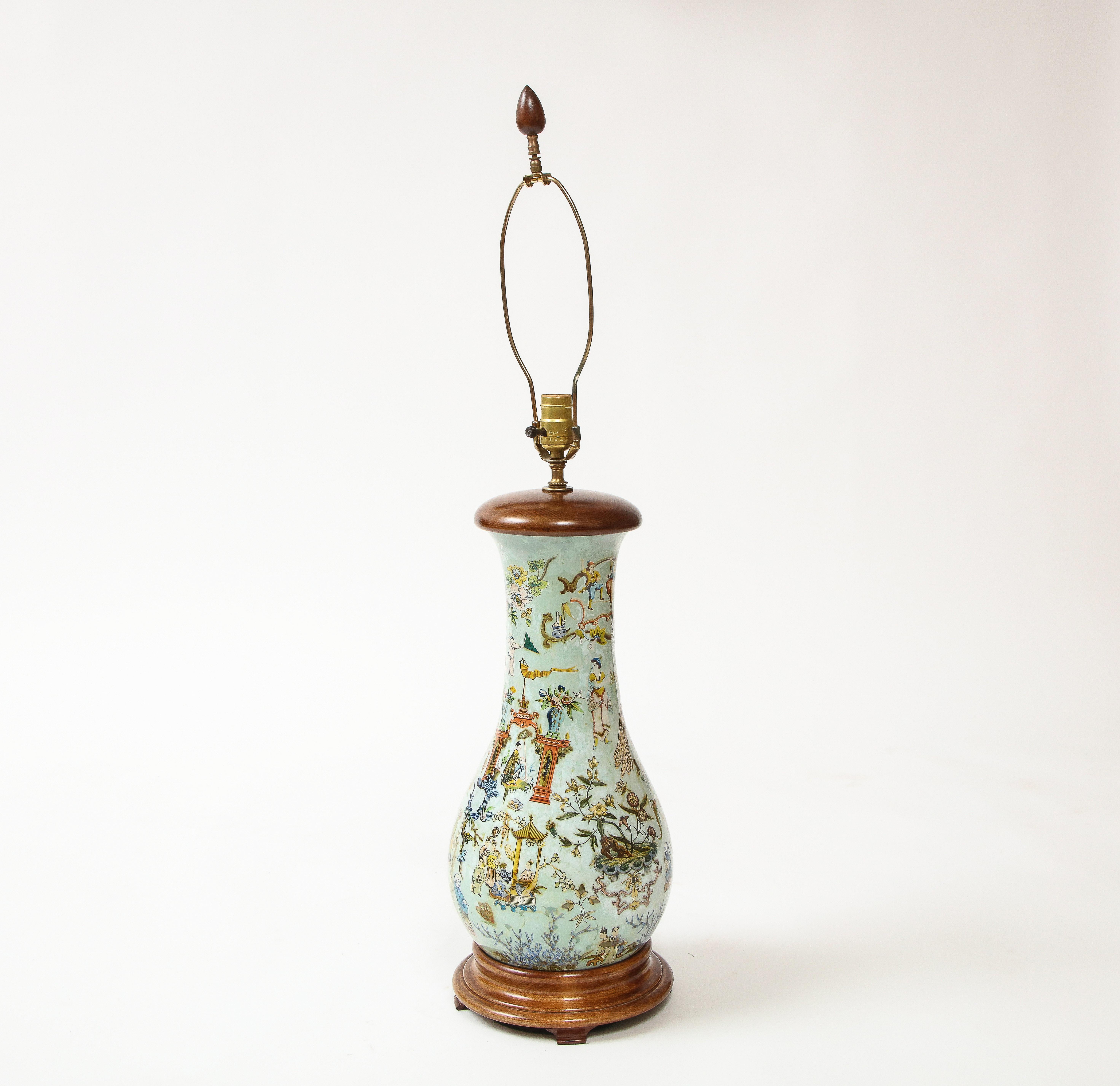 Of pear shape, decorated overall with Chinese-inspired figures at play in a fantasy garden of insects, birds, foliage, and pagodas, on a turned wood plinth base; mounted as a lamp with brass bulb socket and removable harp.