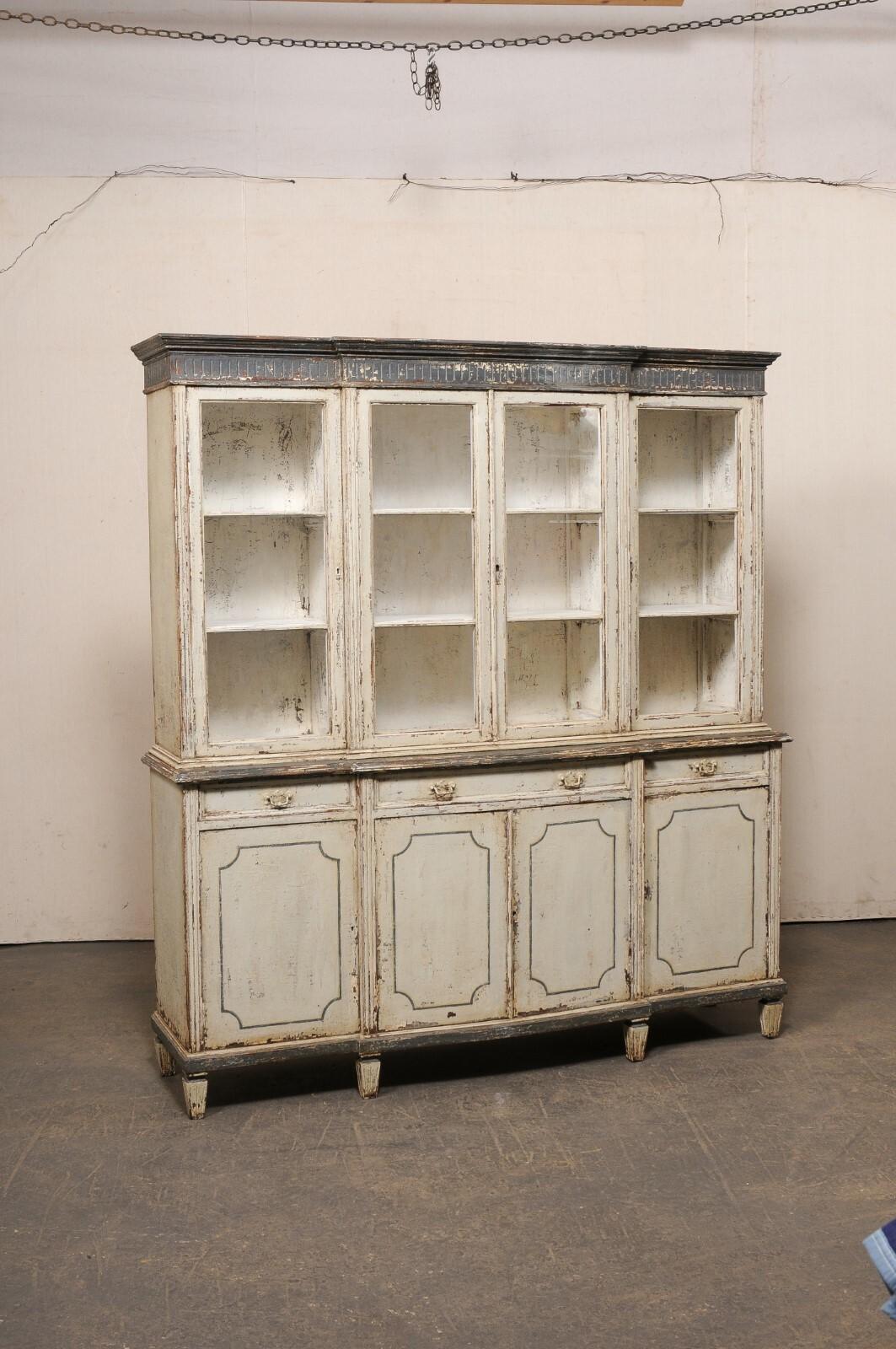A French tall display and storage cabinet from the early 20th century. This antique painted-wood cabinet from France has a shallow break-front design along the front, with a stack molded cornice with fluted carvings beneath. The upper cabinet houses