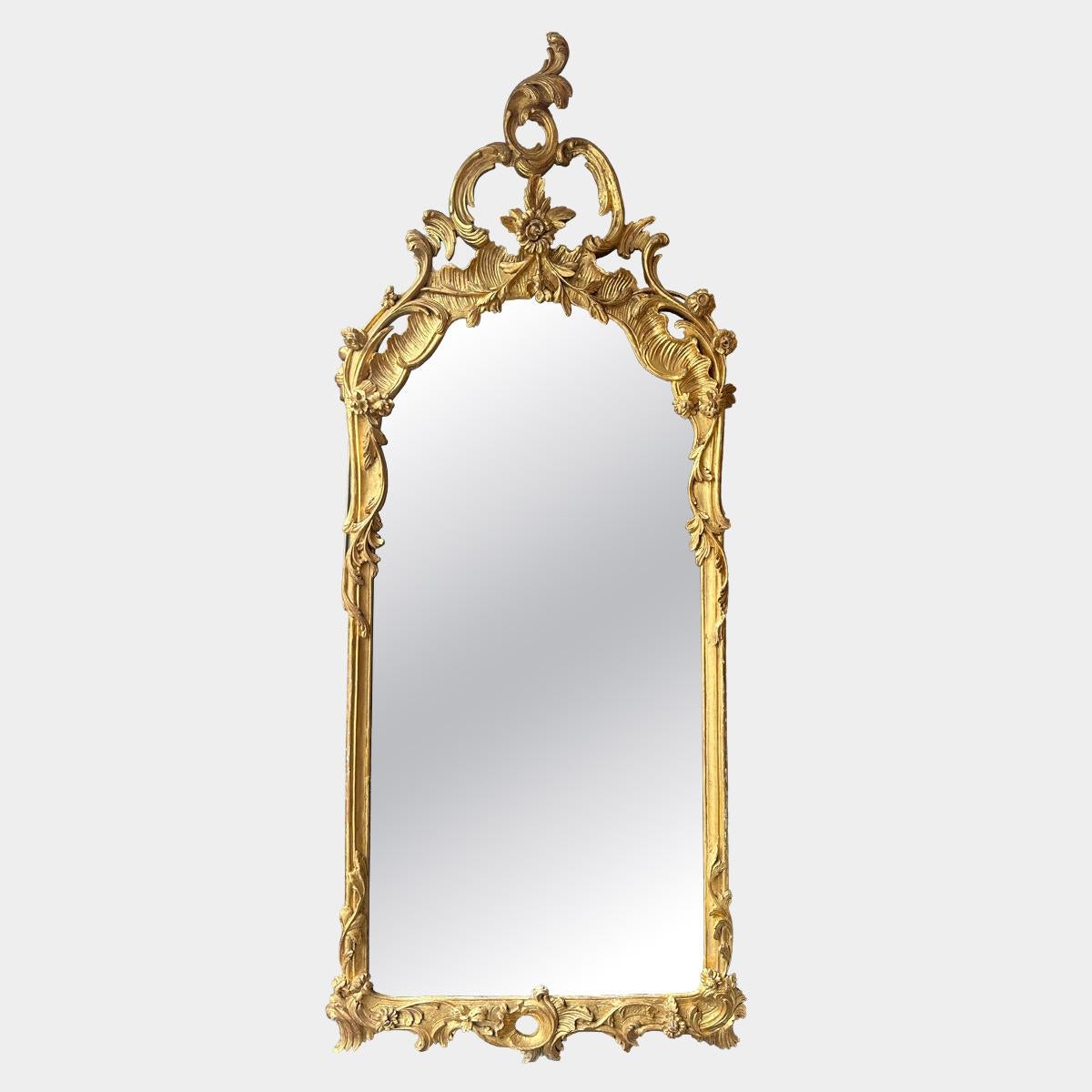 Miroir de grande taille, en bois doré, de style géorgien anglais, avec une plaque de miroir postérieure. Le cadre est décoré d'un écusson d'acanthes et de fleurs qui retombent sur les épaules festonnées. Des feuillages et des acanthes descendent le