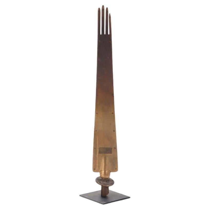 A tall nickel over brass French glove form mold sculpture on an iron stand.