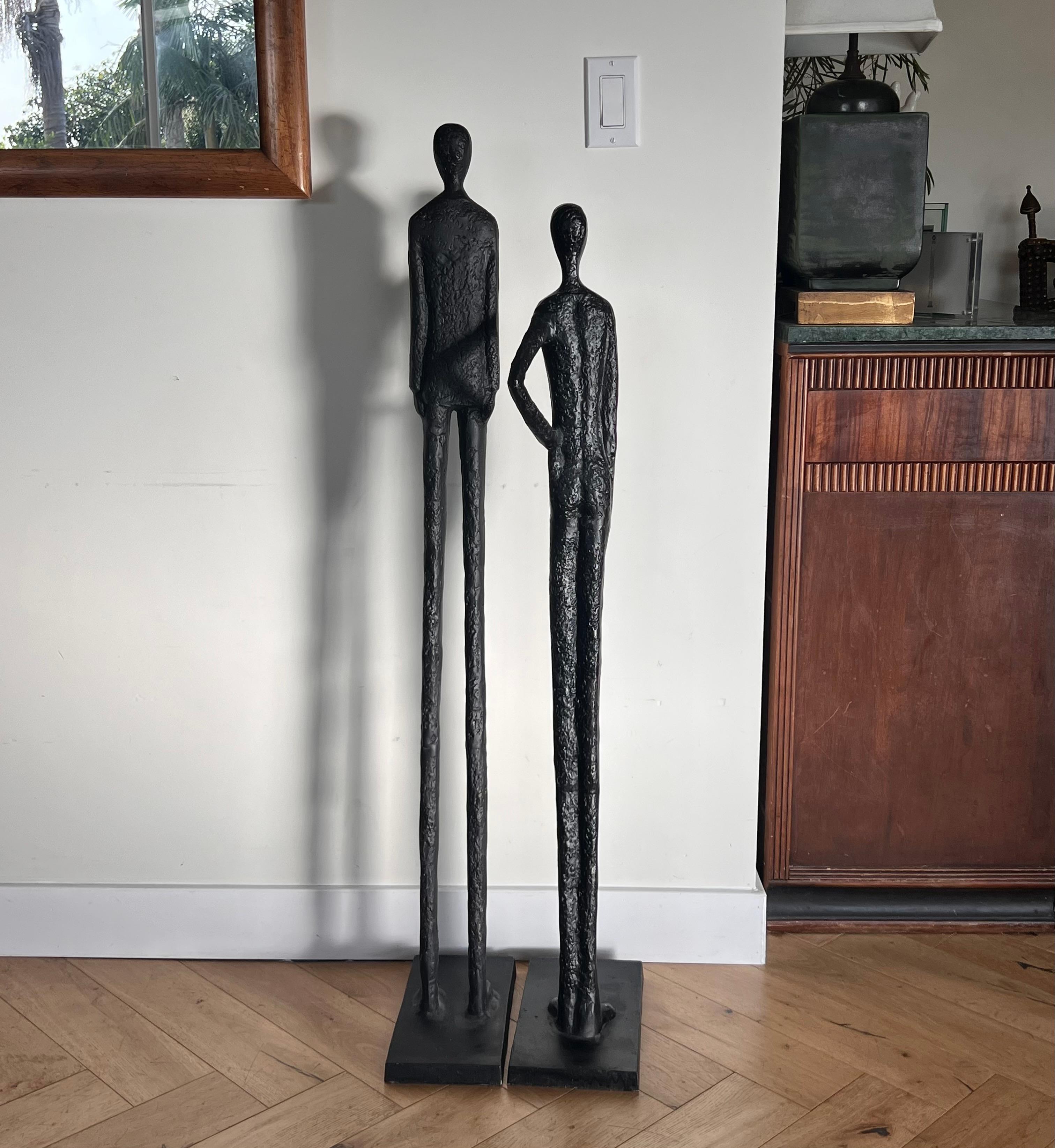 A pair of Giacometti style sculptures, in the likeness of a man and woman, probably late 20th century. These are made to look like hand-carved iron but are actually a lesser, lighter metal - perhaps aluminum or titanium - and then ebonized. Each
